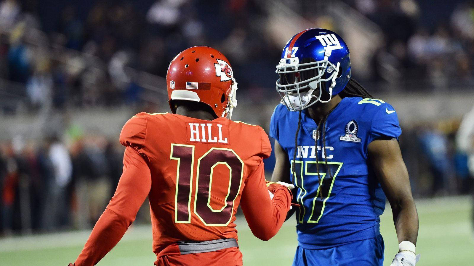 Tyreek Hill 桌布 壁紙 — 兩名身穿紅藍球衣的NFL球員在明亮的燈光下於球場上握手。