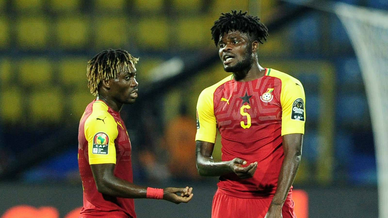 Ghana 桌布 壁紙 — 兩名身穿紅黃球衣的迦納足球員在明亮燈光下的球場上激烈交談。