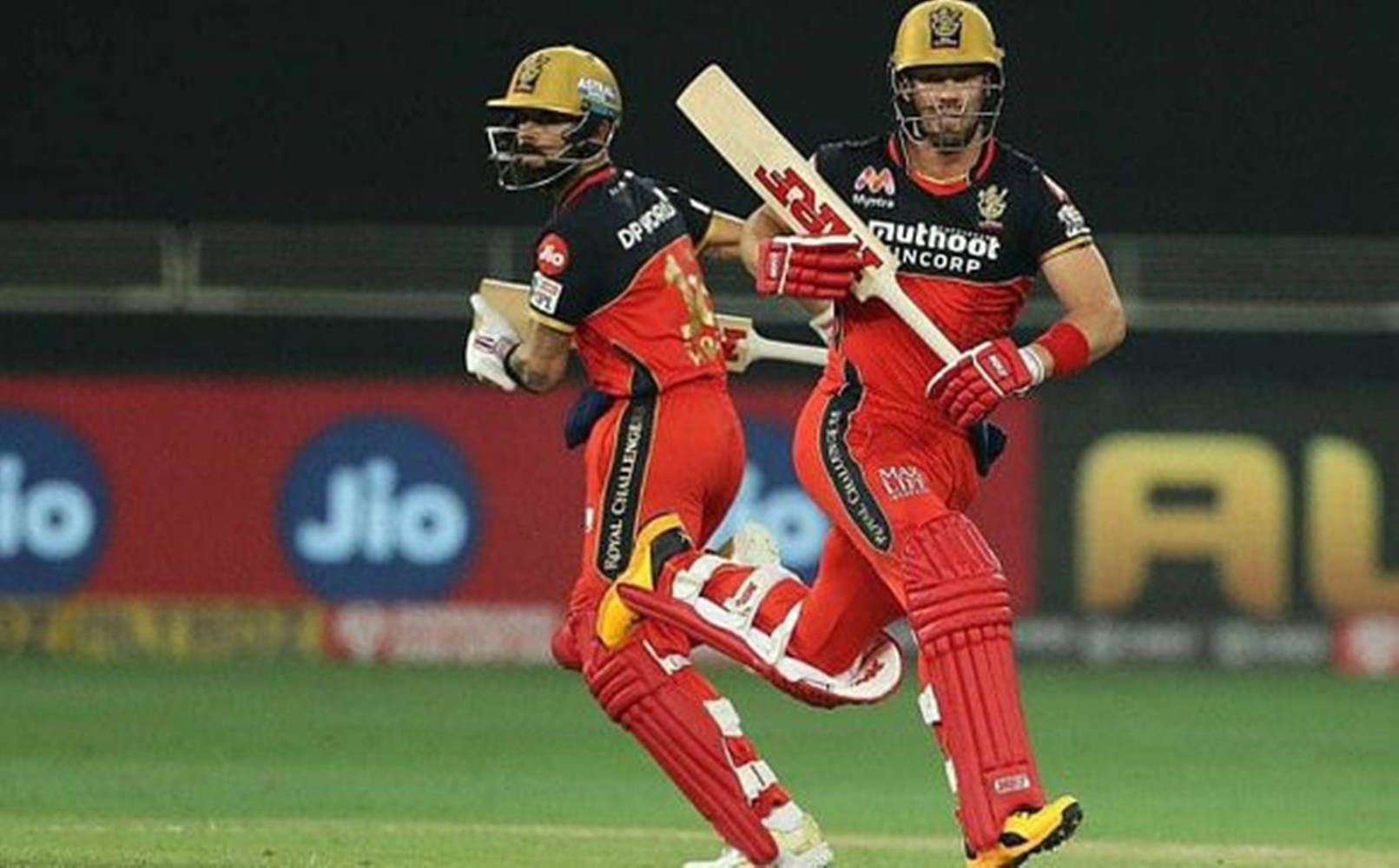 royal challengers bangalore 桌布 壁紙 — 兩名身穿紅黑球衣的板球運動員在夜間比賽中於球場燈光下慶祝得分。