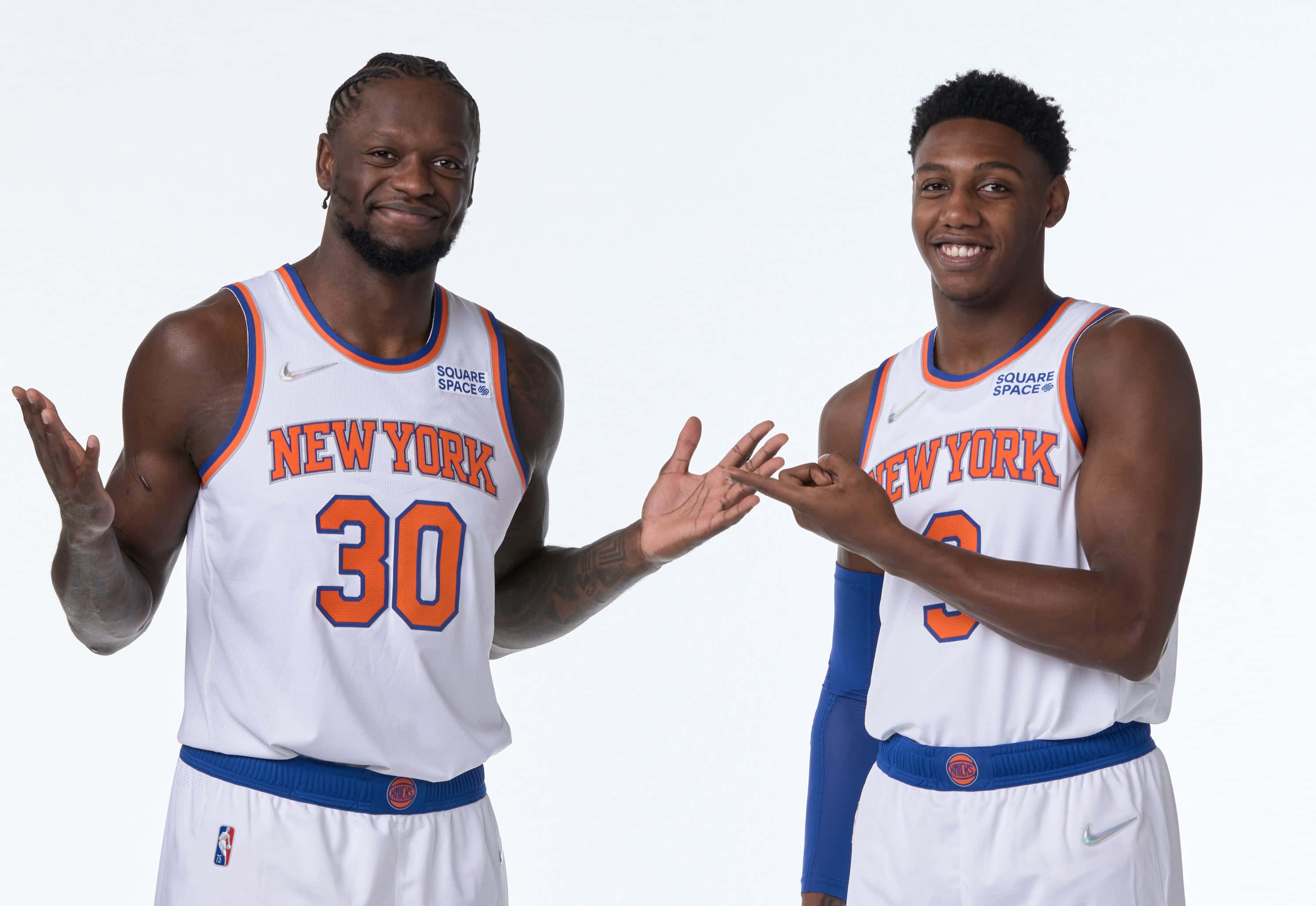 Knicks 桌布 壁紙 — 兩名身穿紐約尼克隊球衣的籃球運動員面帶微笑，在白色背景前張開雙手擺姿勢。