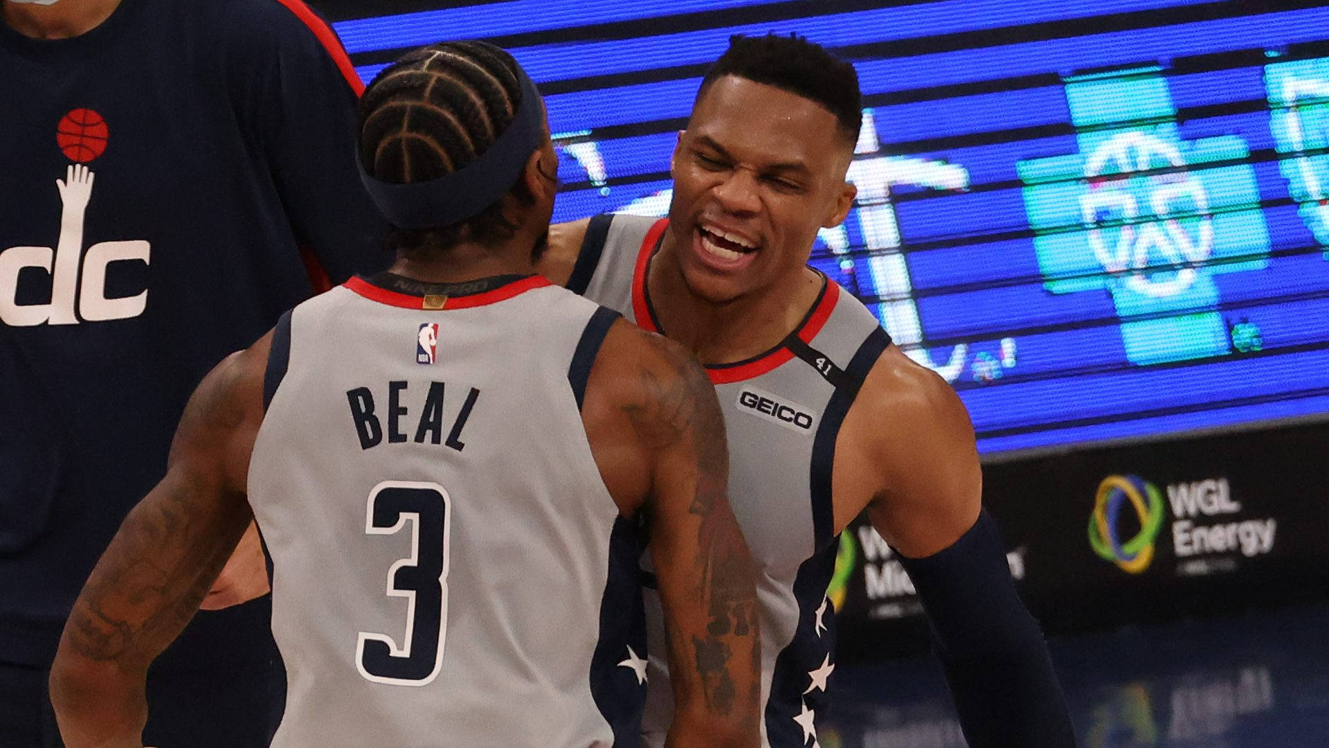 Bradley Beal 桌布 壁紙 — 兩名身穿華盛頓巫師隊球衣的籃球運動員在燈光明亮的球場上熱烈慶祝，身後有電子記分牌。