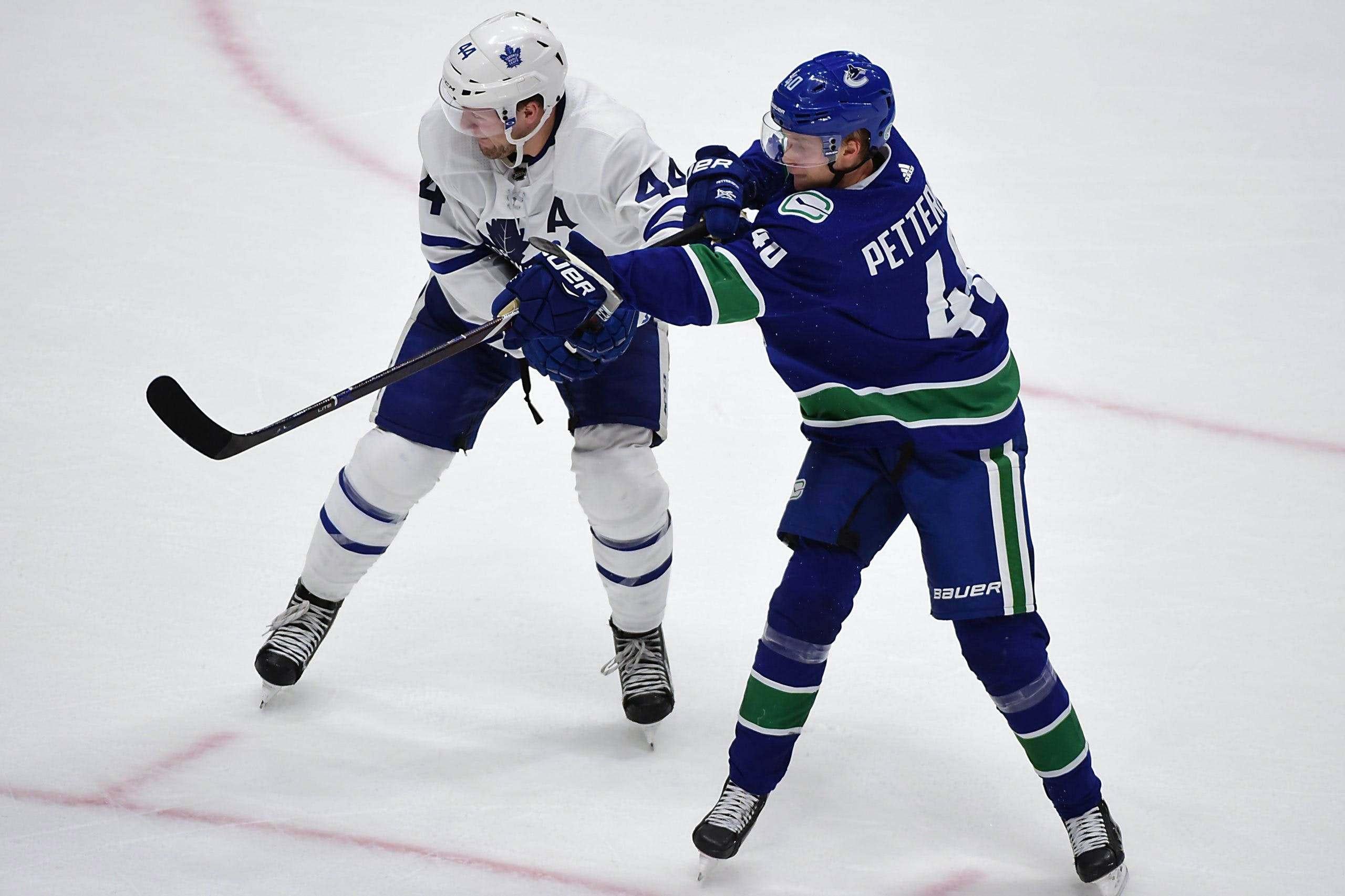 hockey 桌布 壁紙 — 兩名身穿藍白球衣的冰球運動員在明亮的冰面上激烈比賽中爭奪控球權。