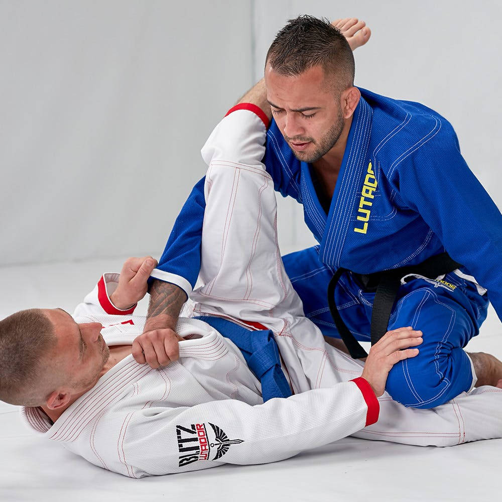 martial arts 桌布 壁紙 — 兩名身穿藍白色柔道服的男人在白色軟墊上激烈纏鬥，進行巴西柔術比賽。