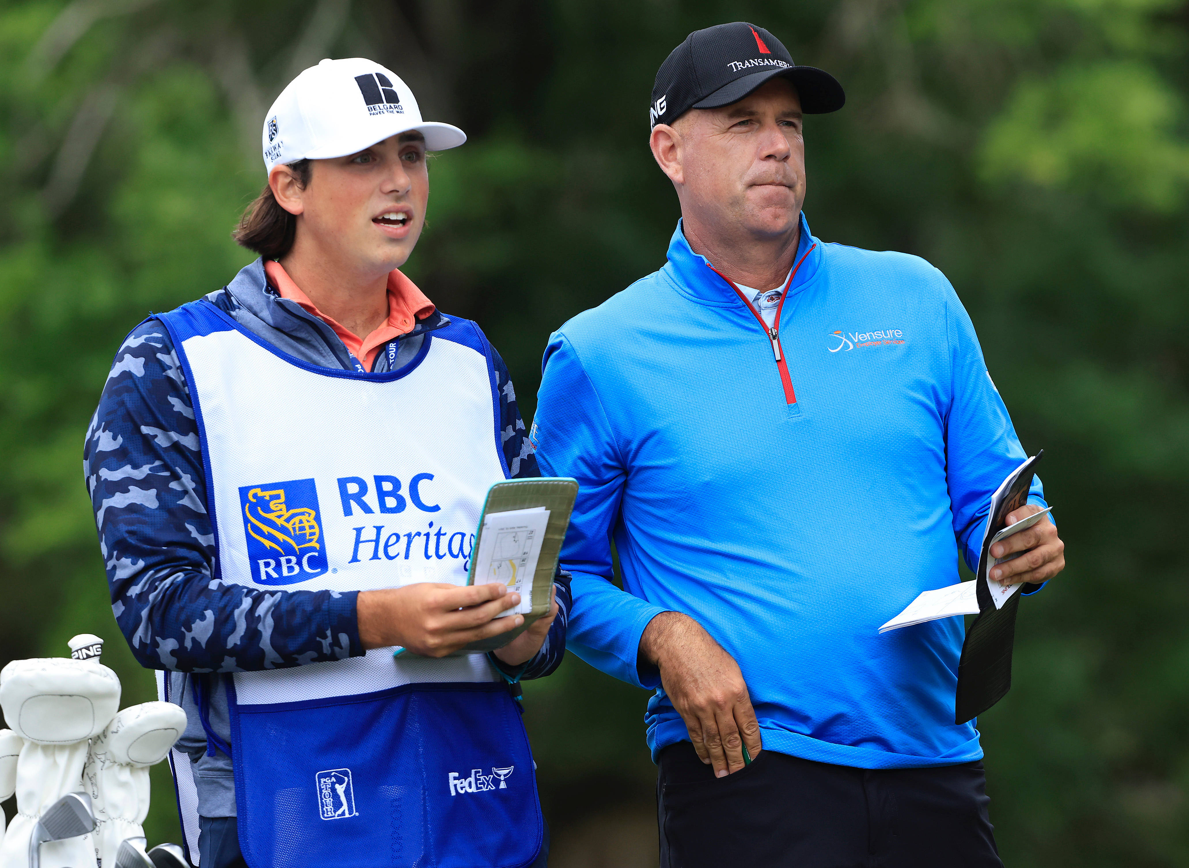 高爾夫 桌布 壁紙 — 兩名身穿藍色RBC Heritage裝備的高爾夫球手站在鬱鬱蔥蔥的綠色球場上，身後有樹木。