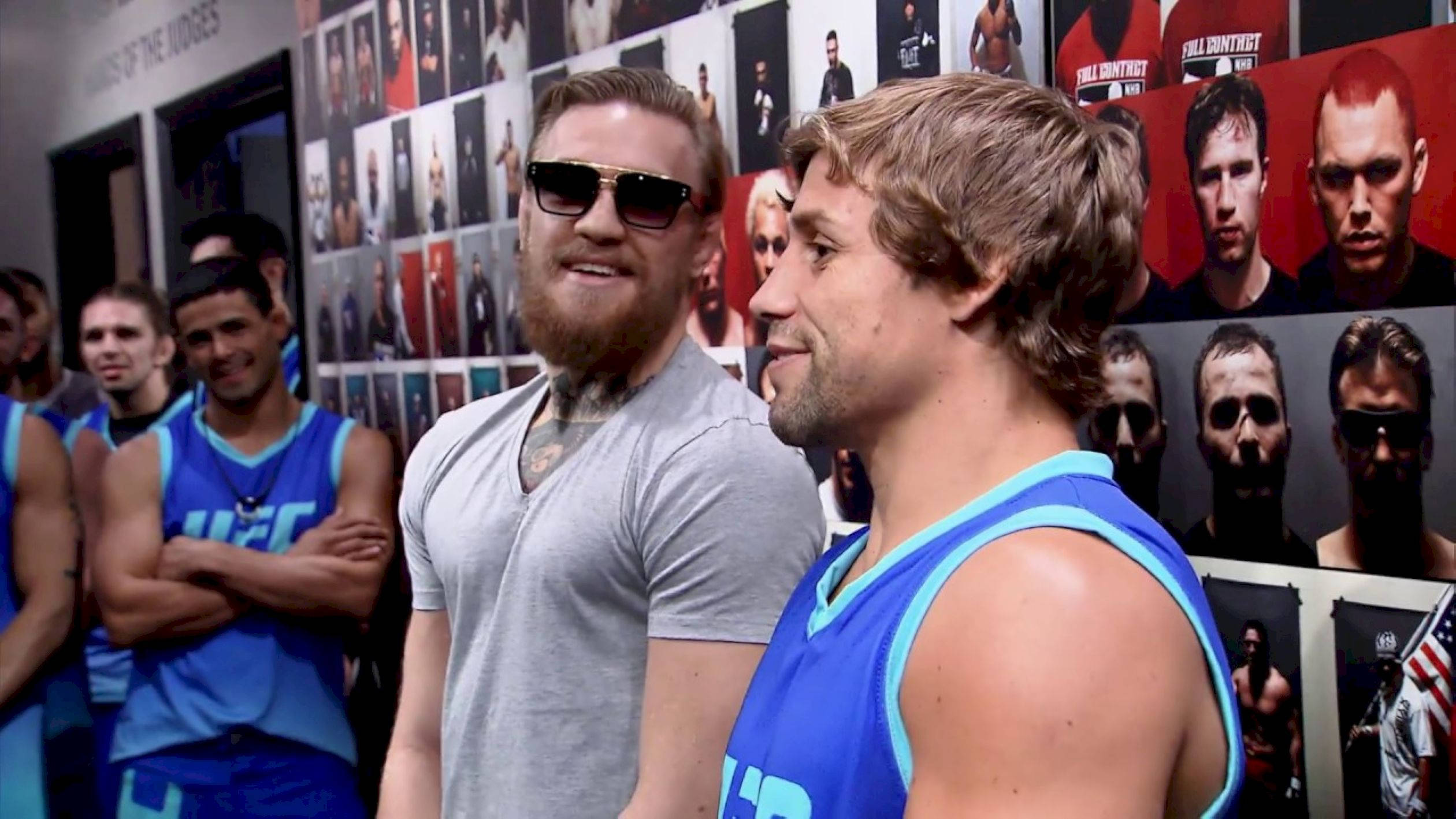UFC 桌布 壁紙 — 兩名身穿藍色UFC裝備的拳手站在一面佈滿拳手肖像的牆前。