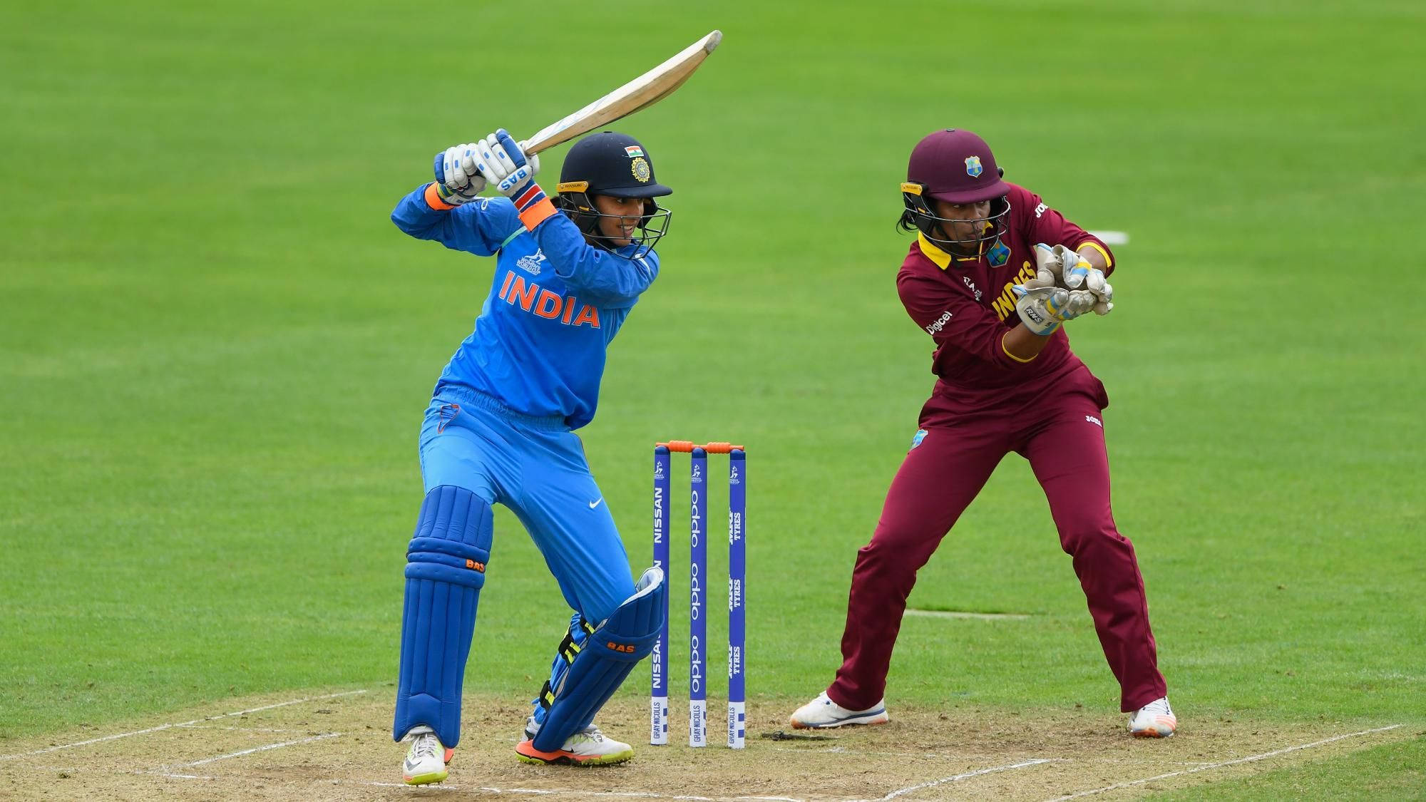 Smriti Mandhana 桌布 壁紙 — 兩名身穿藍色和栗色球衣的板球運動員在充滿活力的綠色場地上比賽時高度專注。