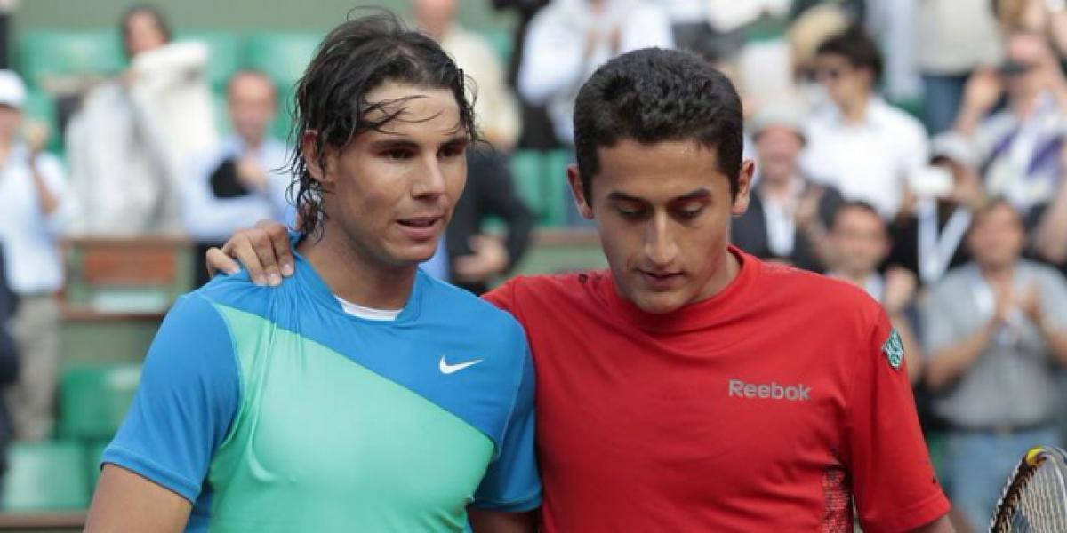 運動 桌布 壁紙 — 兩名身穿藍色和紅色球衣的男網球選手在球場上靠近站立，身後有綠色座位上的觀眾。