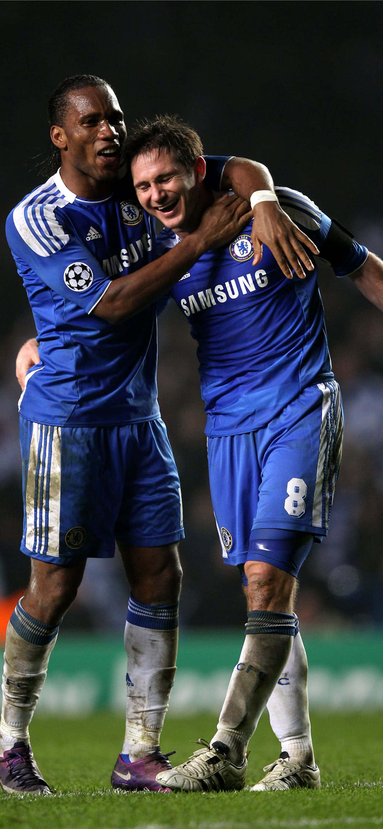 Chelsea iPhone 桌布 壁紙 — 兩名身穿藍色球衣的切爾西足球員在夜間燈光球場上以喜悅的擁抱慶祝進球。