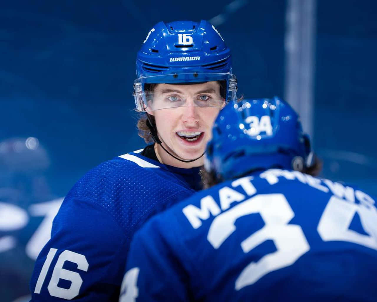 auston matthews 桌布 壁紙 — 兩名身穿藍色球衣的曲棍球運動員在冰上慶祝，其中一人對著鏡頭咧嘴大笑。