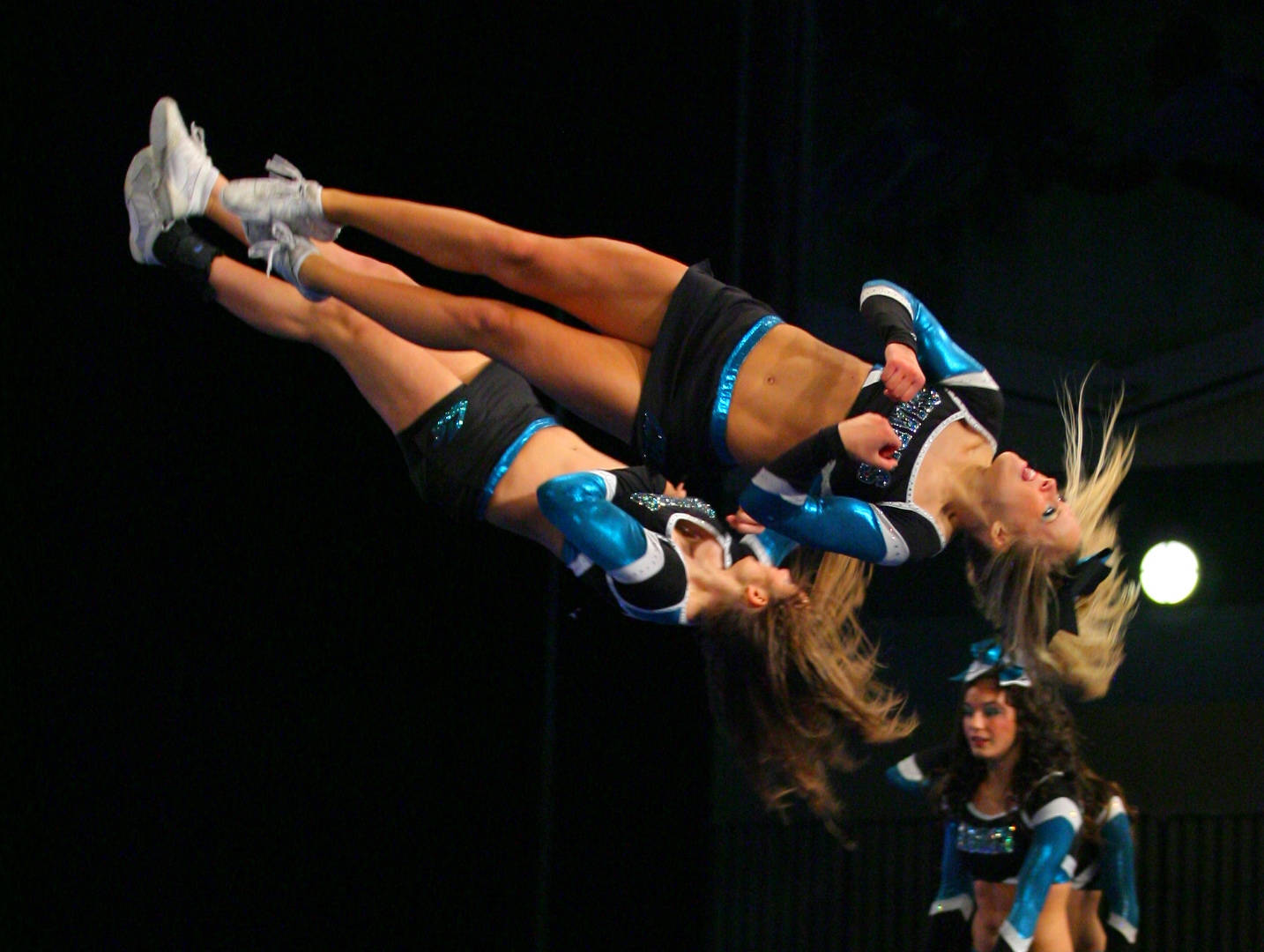 Cheerleader 桌布 壁紙 — 兩名身穿藍黑制服的啦啦隊員在黑暗舞台背景和聚光燈下表演動態空中特技。