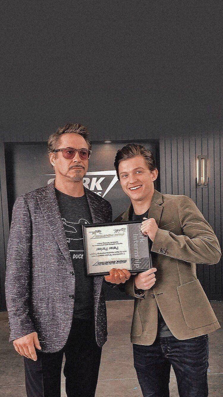 Peter Parker 桌布 壁紙 — 兩名身穿西裝外套的男子微笑著手持裱框獎項，身處現代室內環境，背景有深色牆壁和燈具。