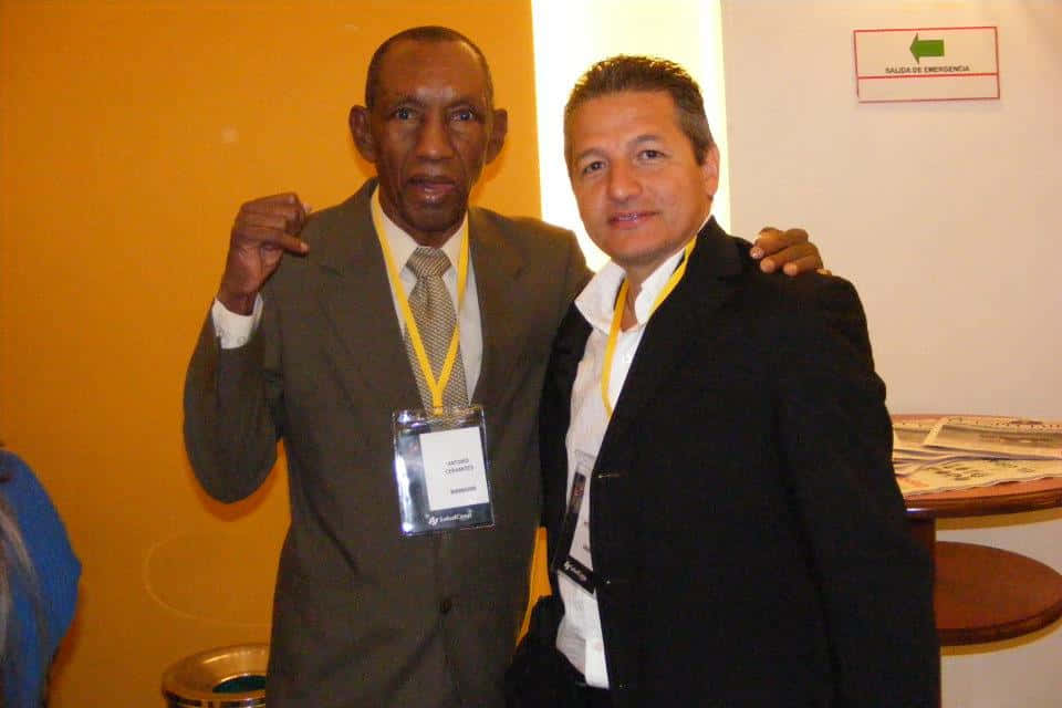 Boxing 桌布 壁紙 — 兩名身穿西裝的男子在一個有黃色牆壁和緊急出口標誌的活動中合影。