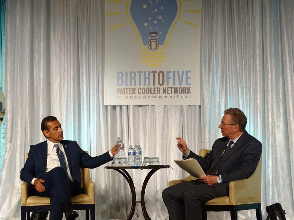 政治 桌布 壁紙 — 兩名身穿西裝的男子在一個正式活動中，於「BirthtoFive Water Cooler Network」橫幅下交談。