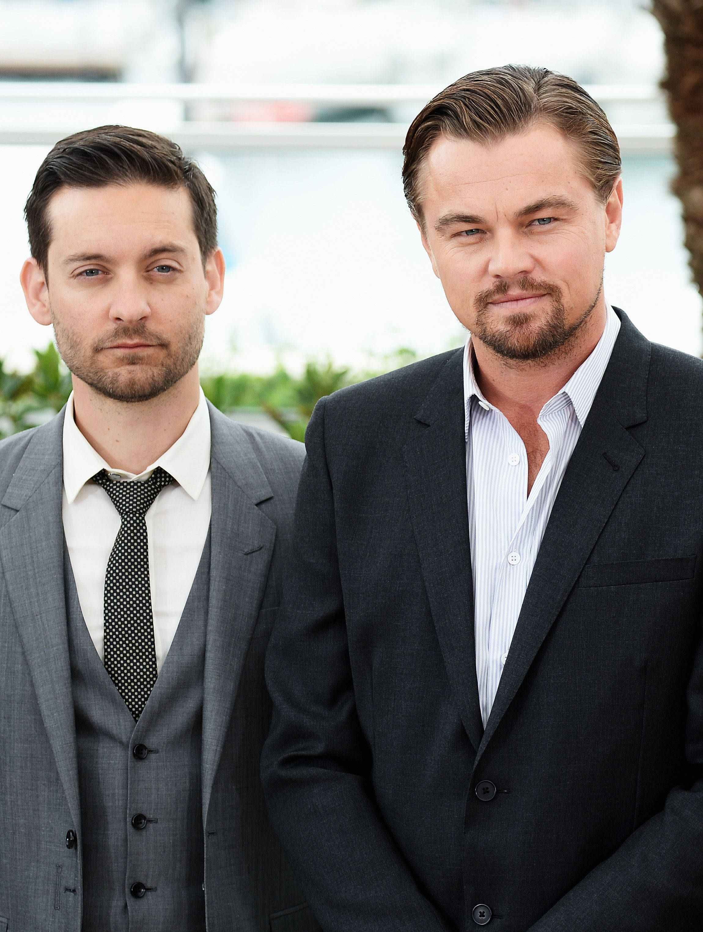 Tobey Maguire 桌布 壁紙 — 兩名身穿西裝的男子在明亮的戶外背景下並肩站立，表情嚴肅。