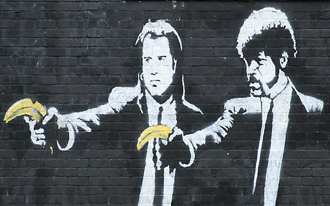 Banksy 桌布 壁紙 — 兩名身穿西裝的男子在磚牆上的黑白街頭壁畫中指向香蕉槍。