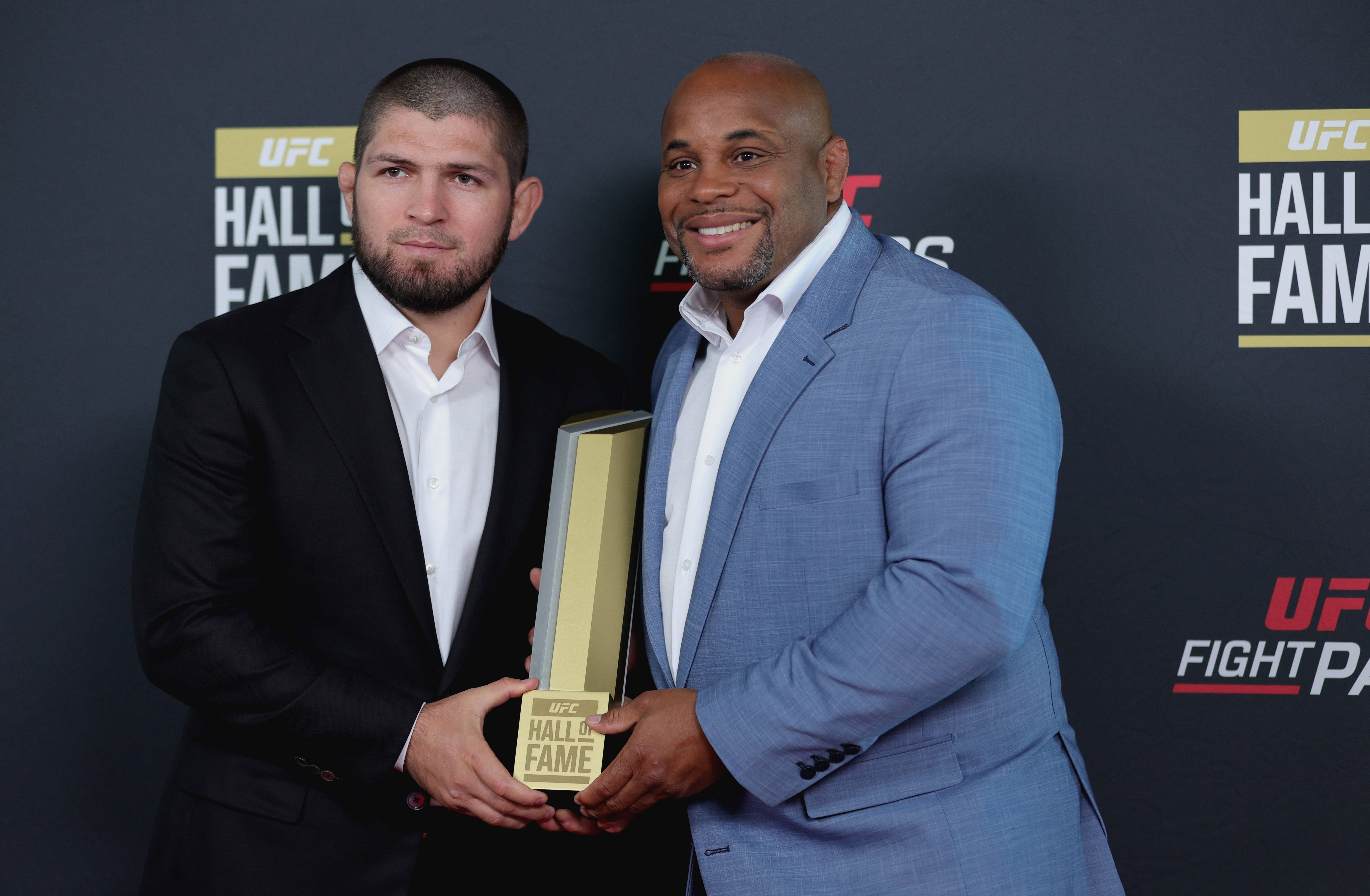 UFC 桌布 壁紙 — 兩名身穿西裝的男子在頒獎典禮上，於品牌背景前舉起UFC名人堂獎盃。