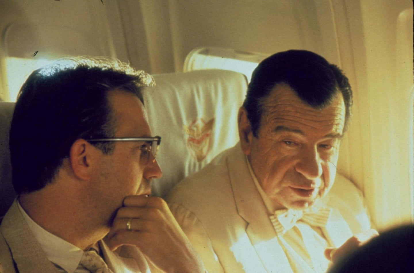 Walter Matthau 桌布 壁紙 — 兩名身穿西裝的男子坐在飛機座位上，一人望向窗外，另一人直視前方，沐浴在溫暖的陽光中。