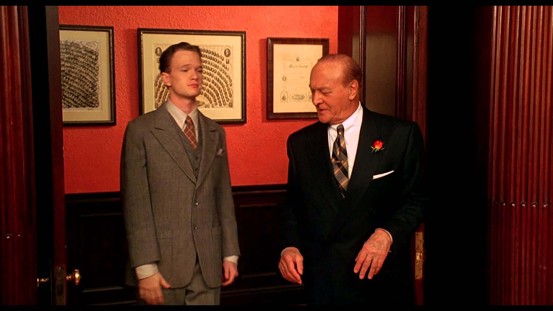 neil patrick harris 桌布 壁紙 — 兩名身穿西裝的男子站在一個燈光溫暖、紅牆掛有證書的房間內。