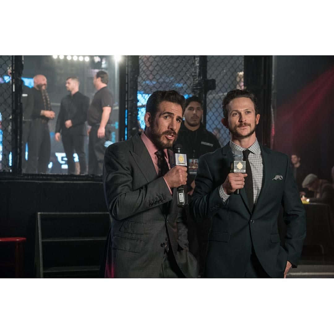 MMA 桌布 壁紙 — 兩名身穿西裝的男性評論員在燈光明亮的MMA八角籠前手持麥克風，背景有拳手。