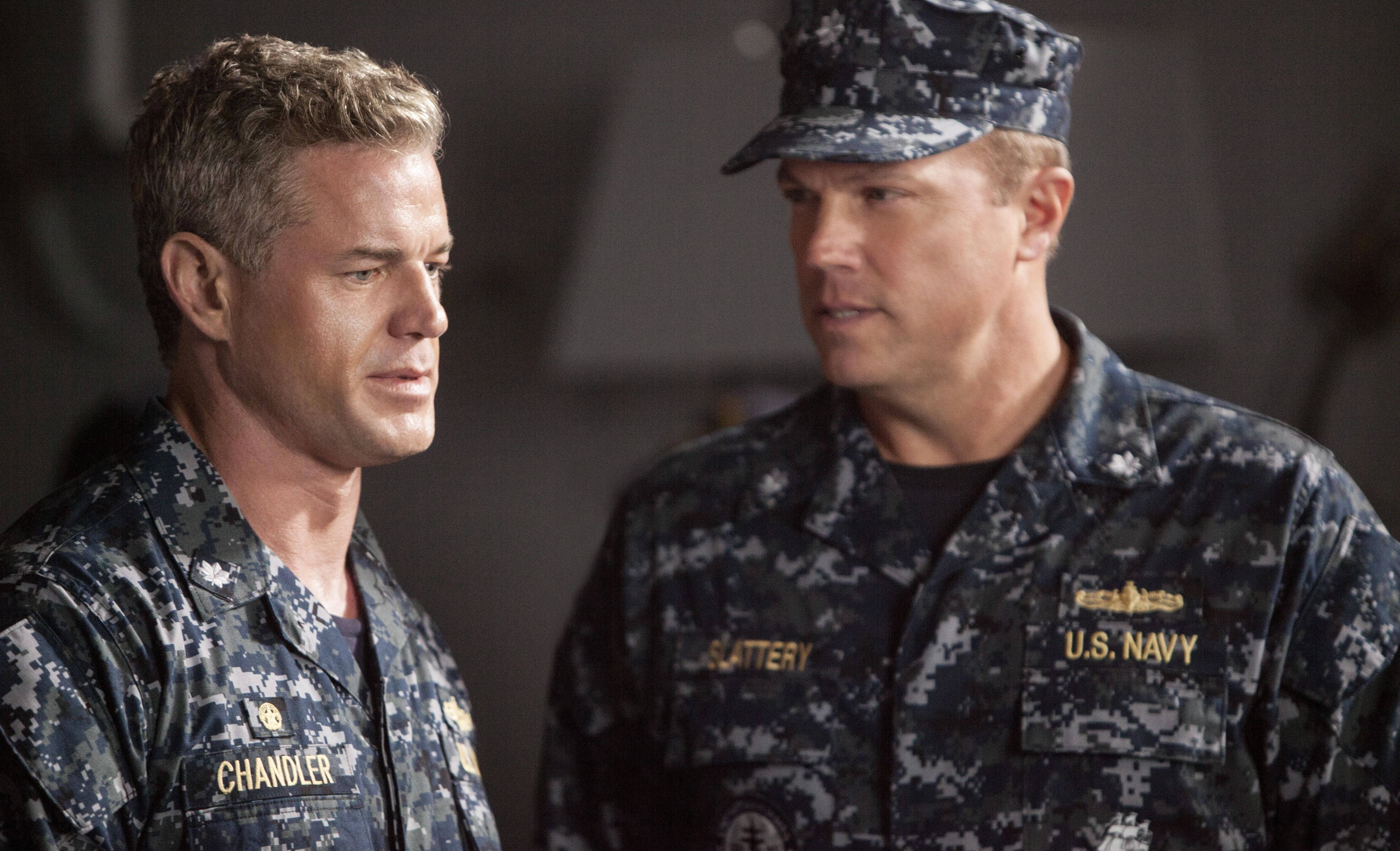 adam baldwin 桌布 壁紙 — 兩名身穿迷彩服的美國海軍軍官在昏暗的燈光下於室內進行嚴肅對話。