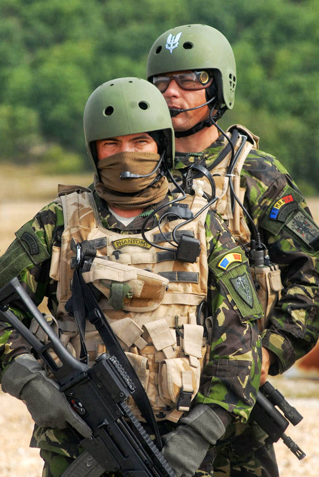 軍事動圖 桌布 壁紙 — 兩名身穿迷彩裝備和頭盔的士兵持步槍警覺地站立，背景是模糊的綠色森林。