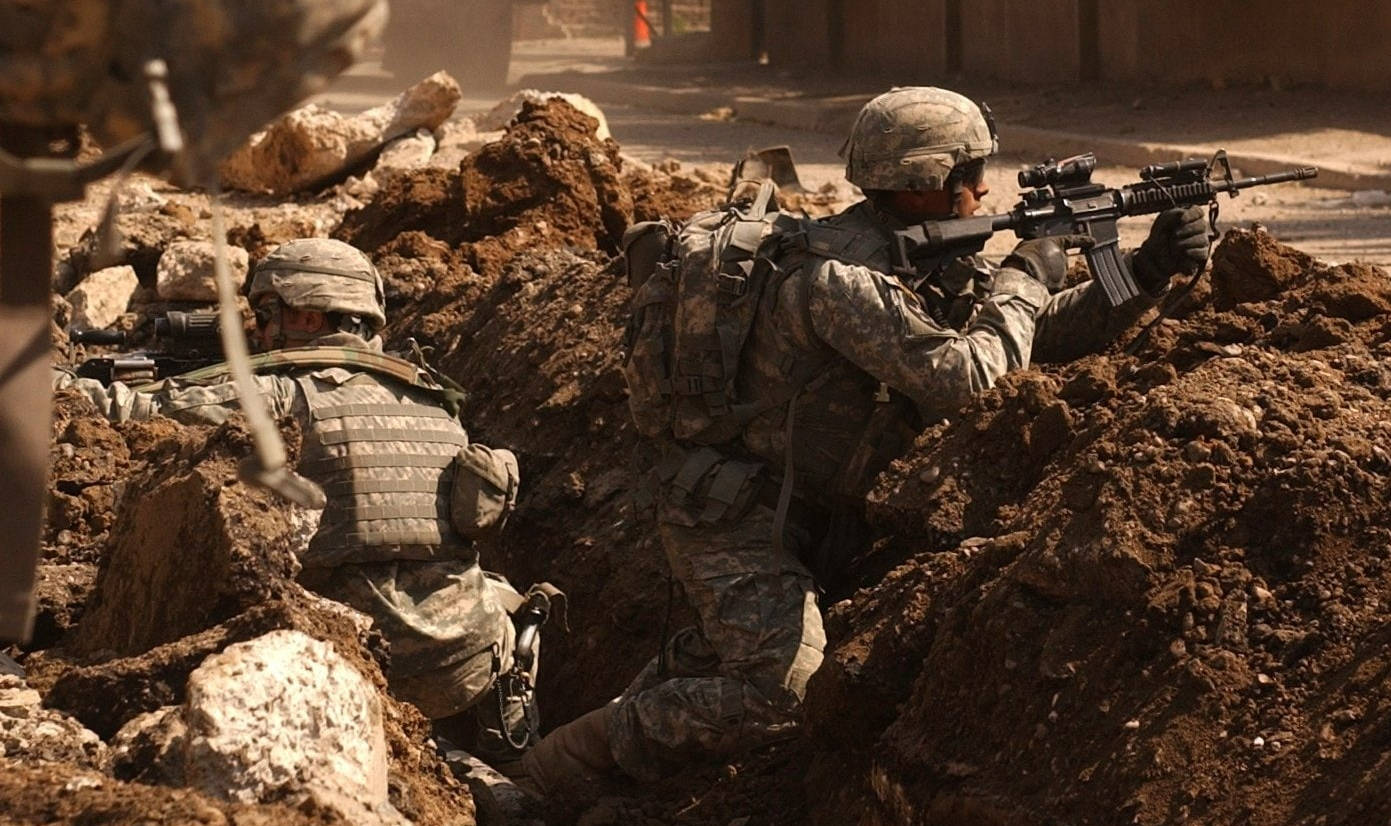 Iraq 桌布 壁紙 — 兩名身穿迷彩裝備的士兵在塵土飛揚的戰場上躲在土堆後面瞄準步槍。
