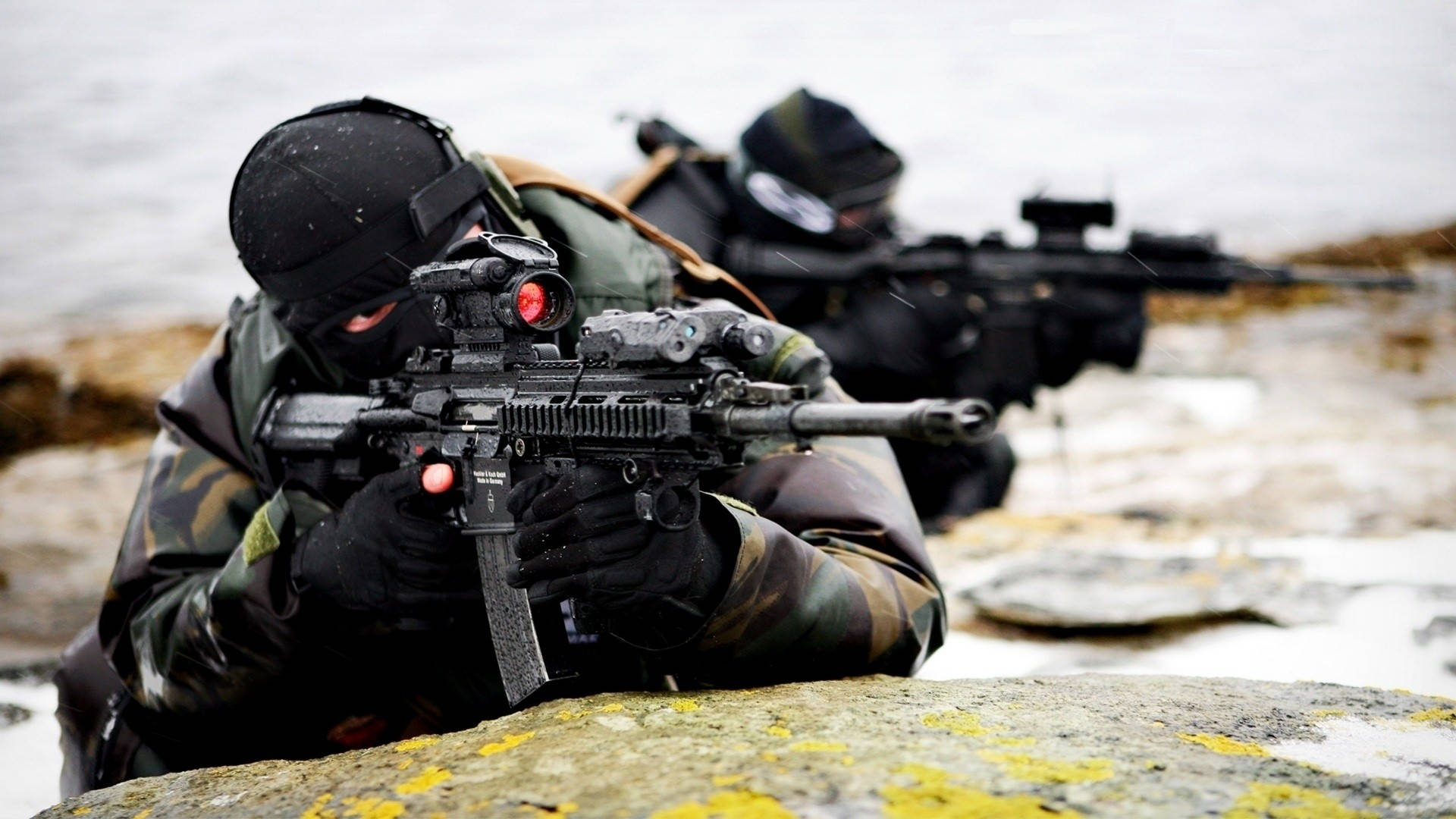 HD Military 桌布 壁紙 — 兩名身穿迷彩裝備的士兵在陰天的雪岸上，從岩石後面用步槍瞄準。