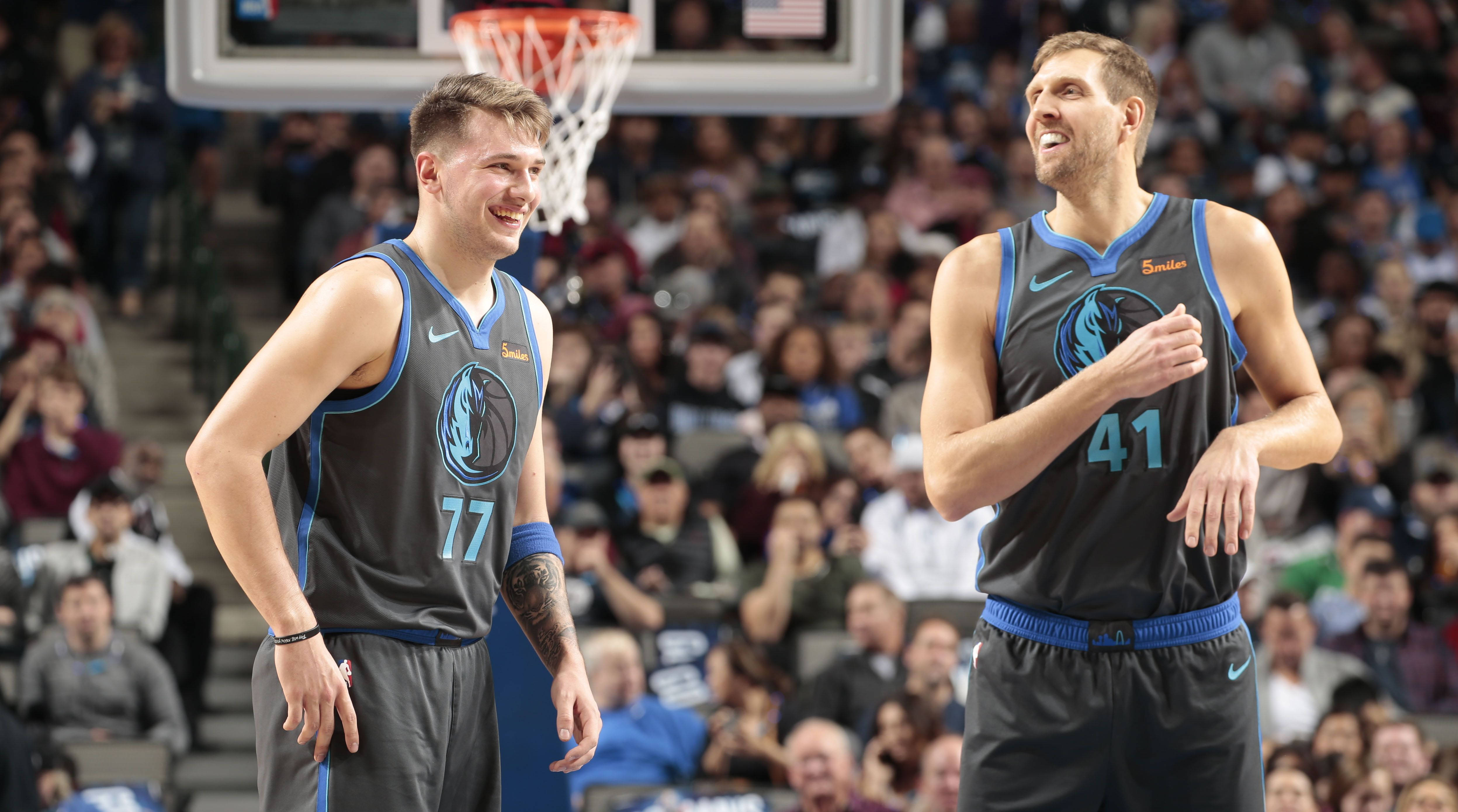 Luka Doncic 桌布 壁紙 — 兩名身穿達拉斯獨行俠隊球衣的籃球運動員在明亮的場館燈光下，背景有觀眾，一起開懷大笑。