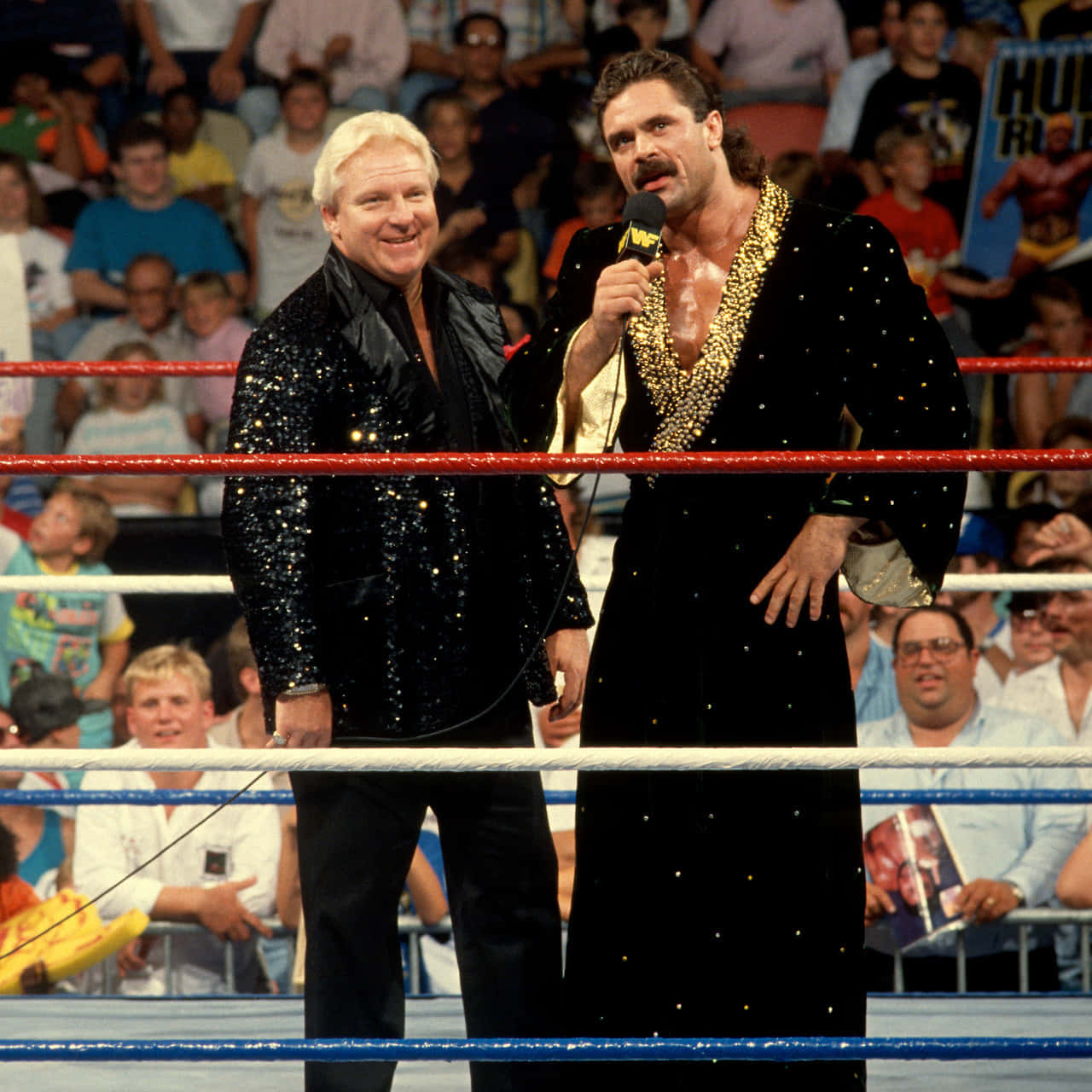 Bobby Heenan 桌布 壁紙 — 兩名身穿閃亮黑色服裝的WWE摔角手站在擂台上，身後是歡呼的人群。