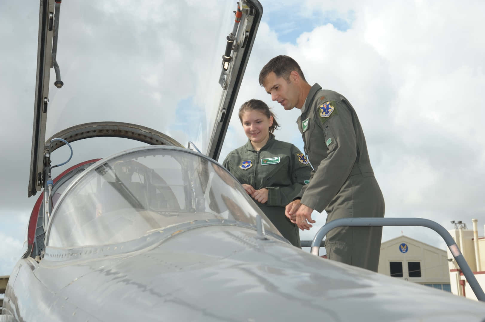 Air Force 桌布 壁紙 — 兩名身穿飛行服的飛行員在多雲的天空下檢查戰鬥機的駕駛艙。