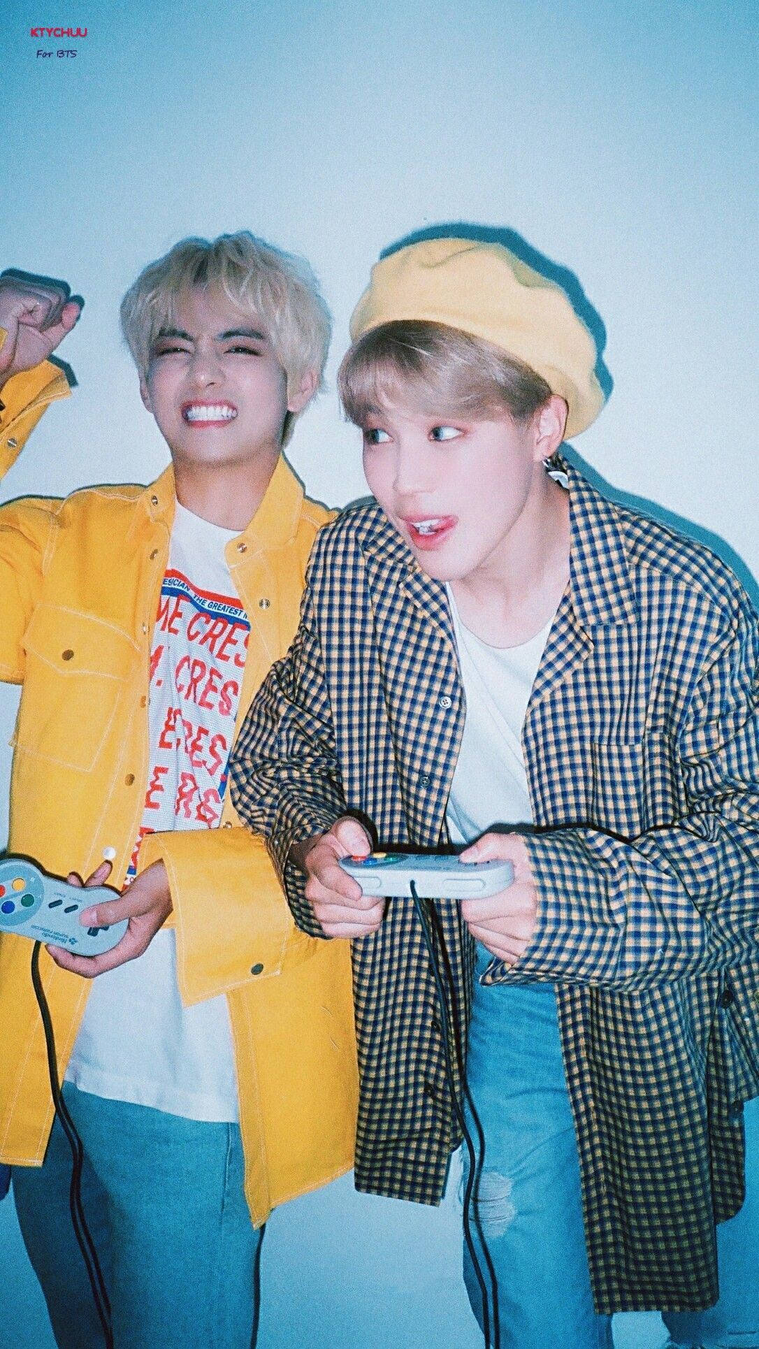 BTS 桌布 壁紙 — 兩名身穿鮮豔黃色和格子服裝的年輕男子，在酷炫的藍色背景下，熱情地使用控制器玩復古電子遊戲。