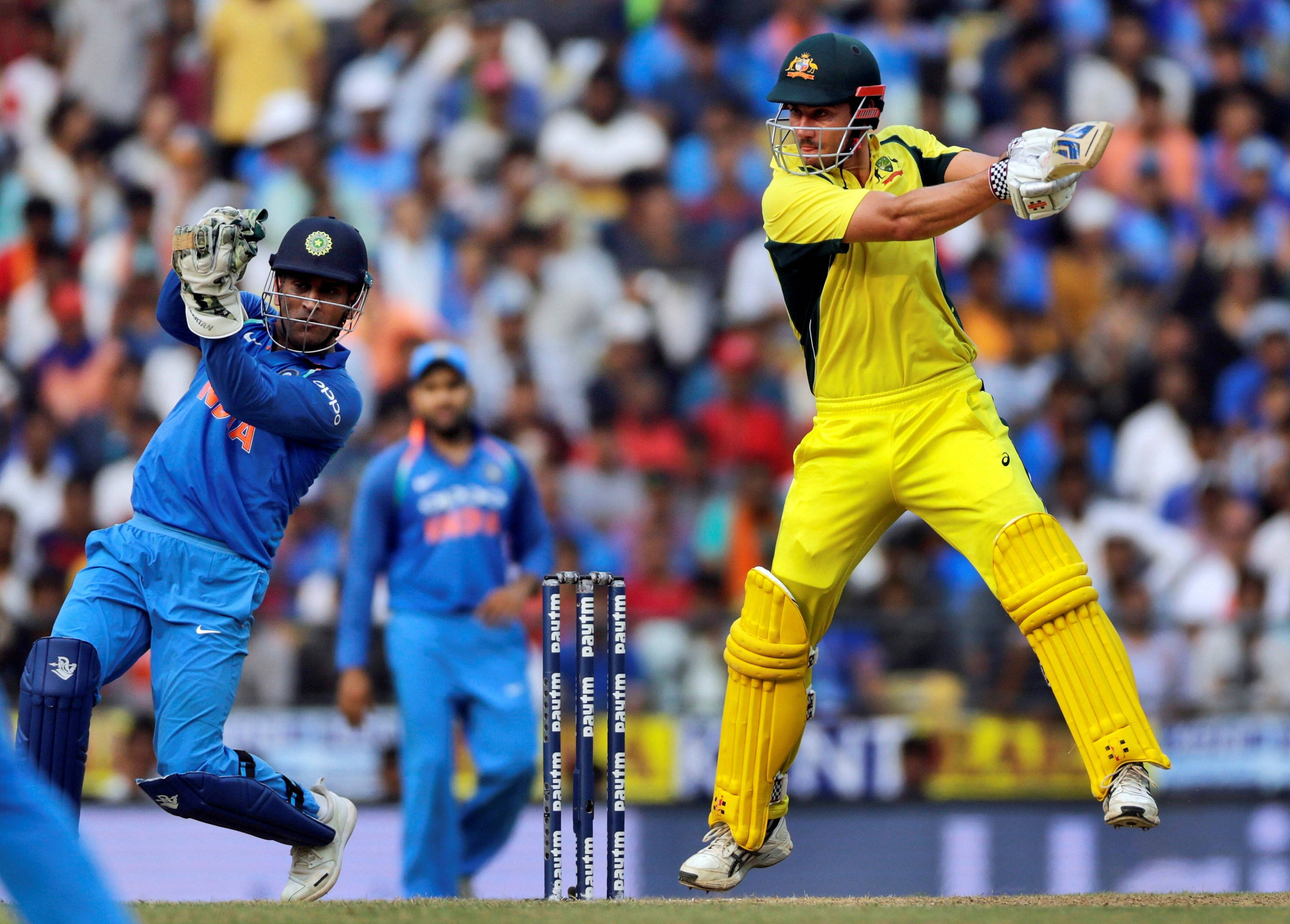 australia cricket 桌布 壁紙 — 兩名身穿鮮豔黃藍色球衣的板球擊球手在擠滿觀眾的體育場比賽中強力揮棒擊球。