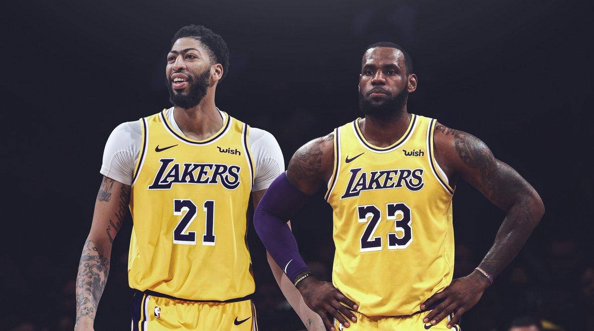 Anthony Davis 桌布 壁紙 — 兩名身穿黃色球衣的湖人籃球運動員自信地站在燈光昏暗的球場上，神情專注。