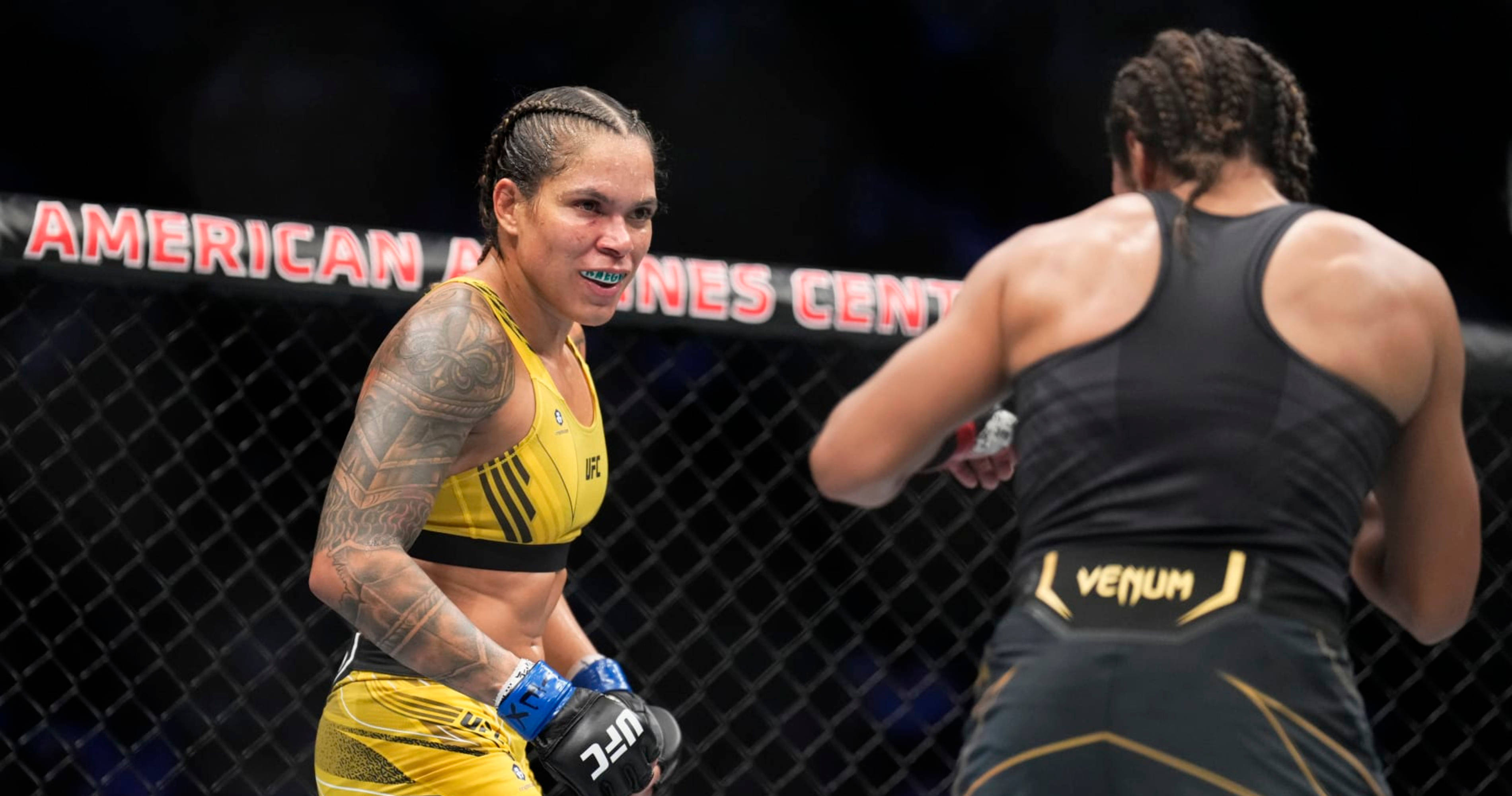 MMA 桌布 壁紙 — 兩名身穿黃黑裝備的女性MMA拳手在美國航空中心的鐵籠內激烈對峙，專注度極高。