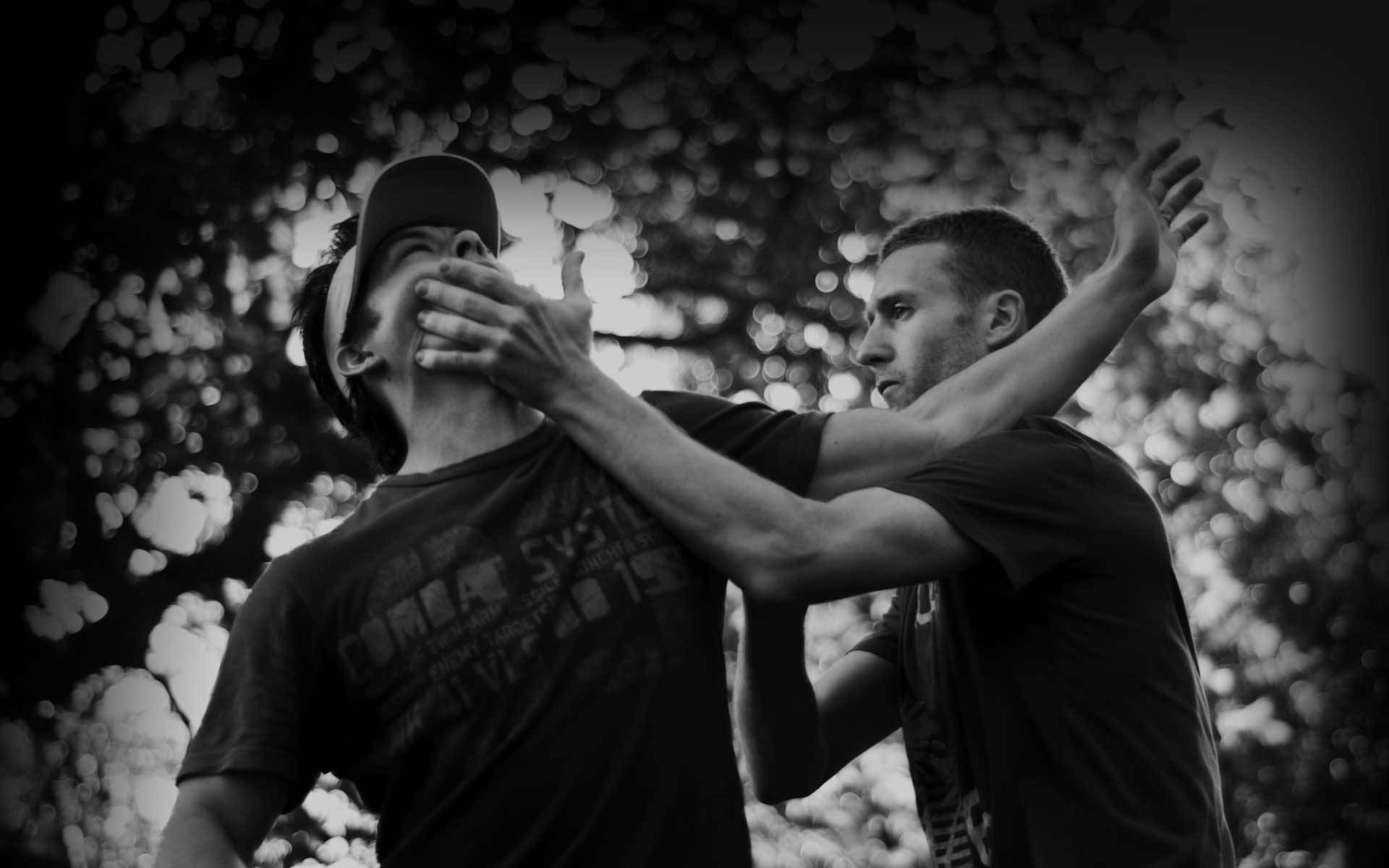 martial arts 桌布 壁紙 — 兩名身穿黑白衣服的男子在模糊的樹葉背景下進行緊張的肢體搏鬥。