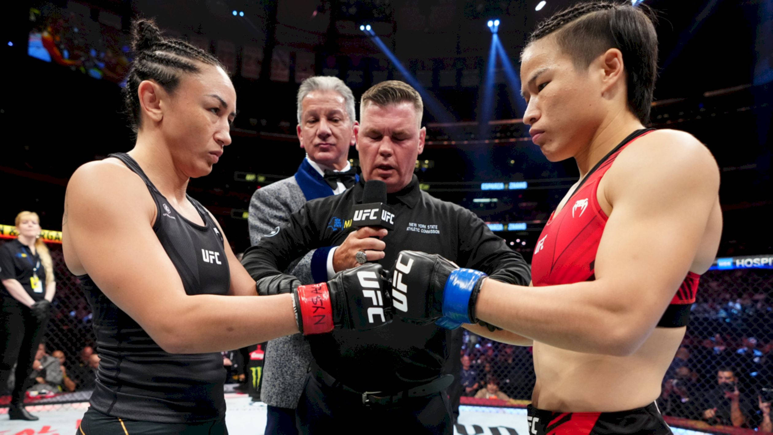 Athletic 桌布 壁紙 — 兩名身穿黑色和紅色裝備的女子UFC拳手在明亮的場館燈光下於八角籠中對峙，中間有一名裁判。