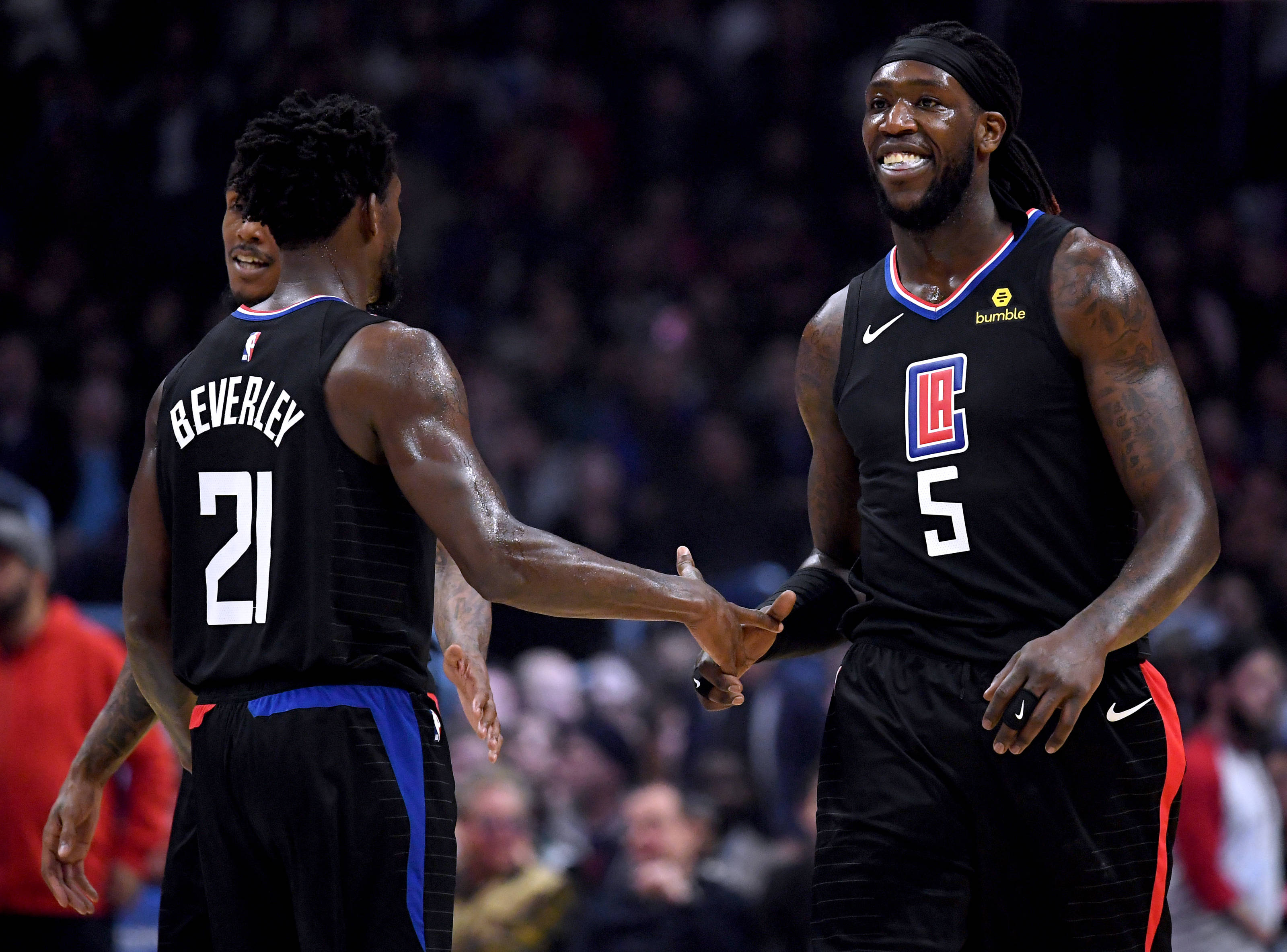 montrezl harrell 桌布 壁紙 — 兩名身穿黑色洛杉磯快艇隊球衣的籃球運動員在燈光明亮的球場上握手，背景是模糊的觀眾。
