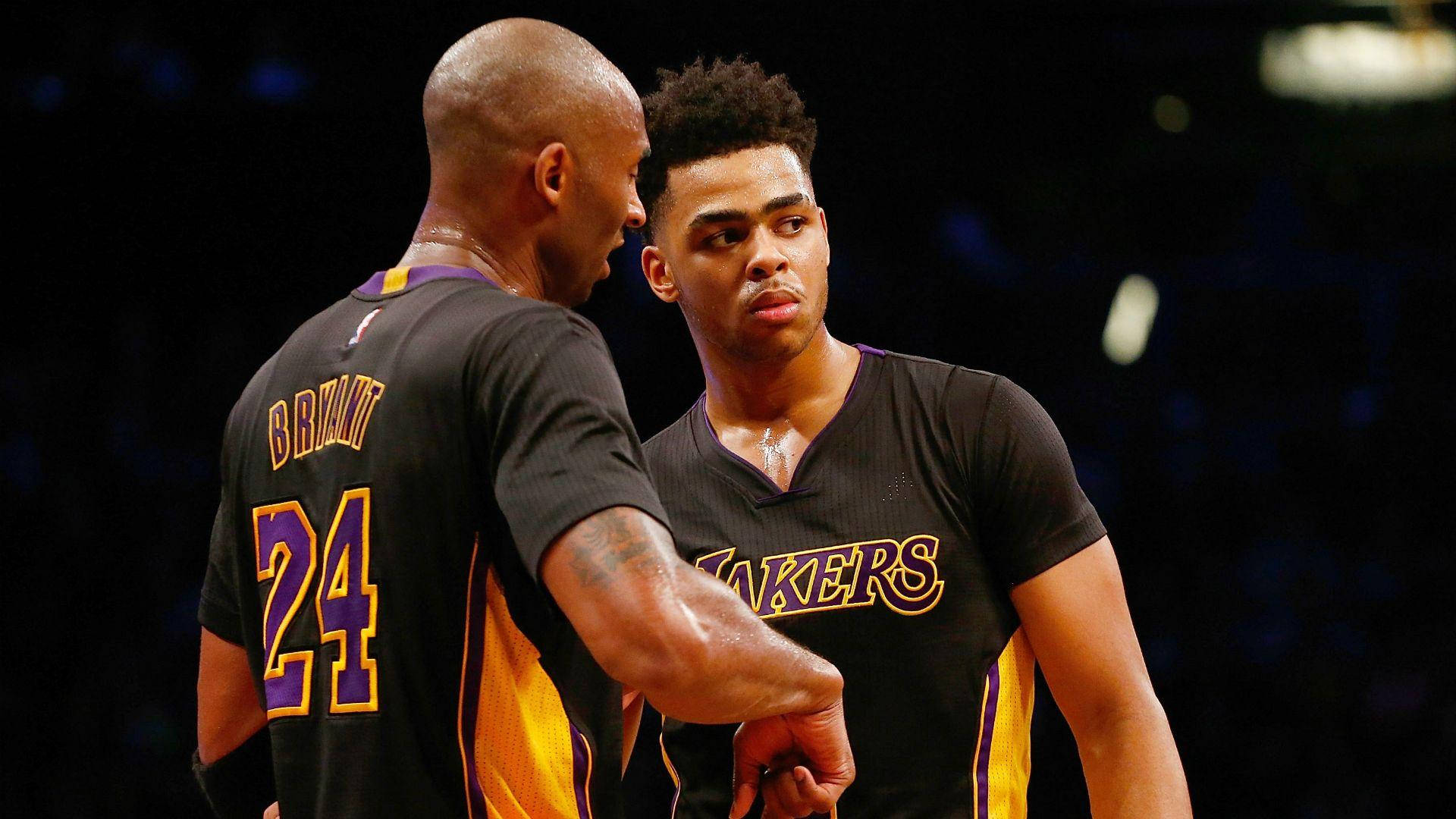 NBA 桌布 壁紙 — 兩名身穿黑色湖人隊球衣的籃球運動員在場館燈光下進行專注的交談。
