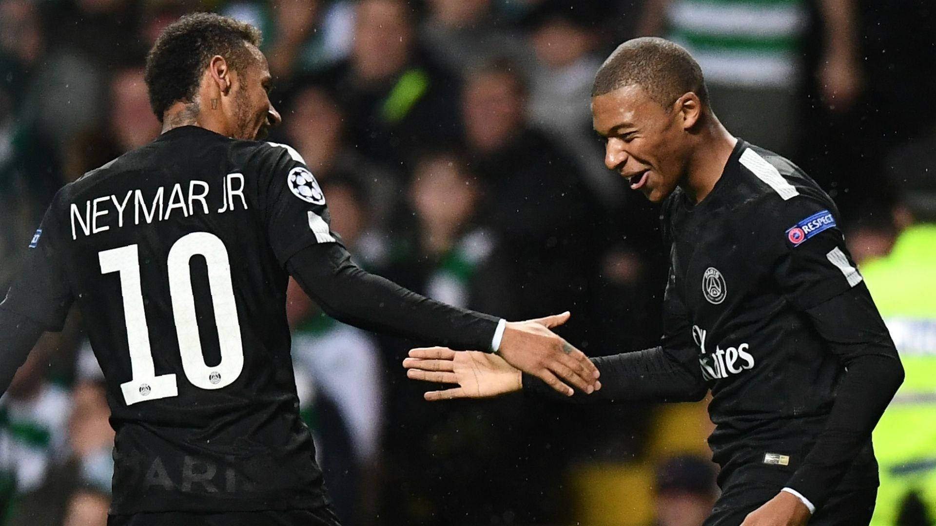 Kylian Mbappe 桌布 壁紙 — 兩名身穿黑色球衣的足球運動員在雨夜球場上，在體育場燈光下握手。