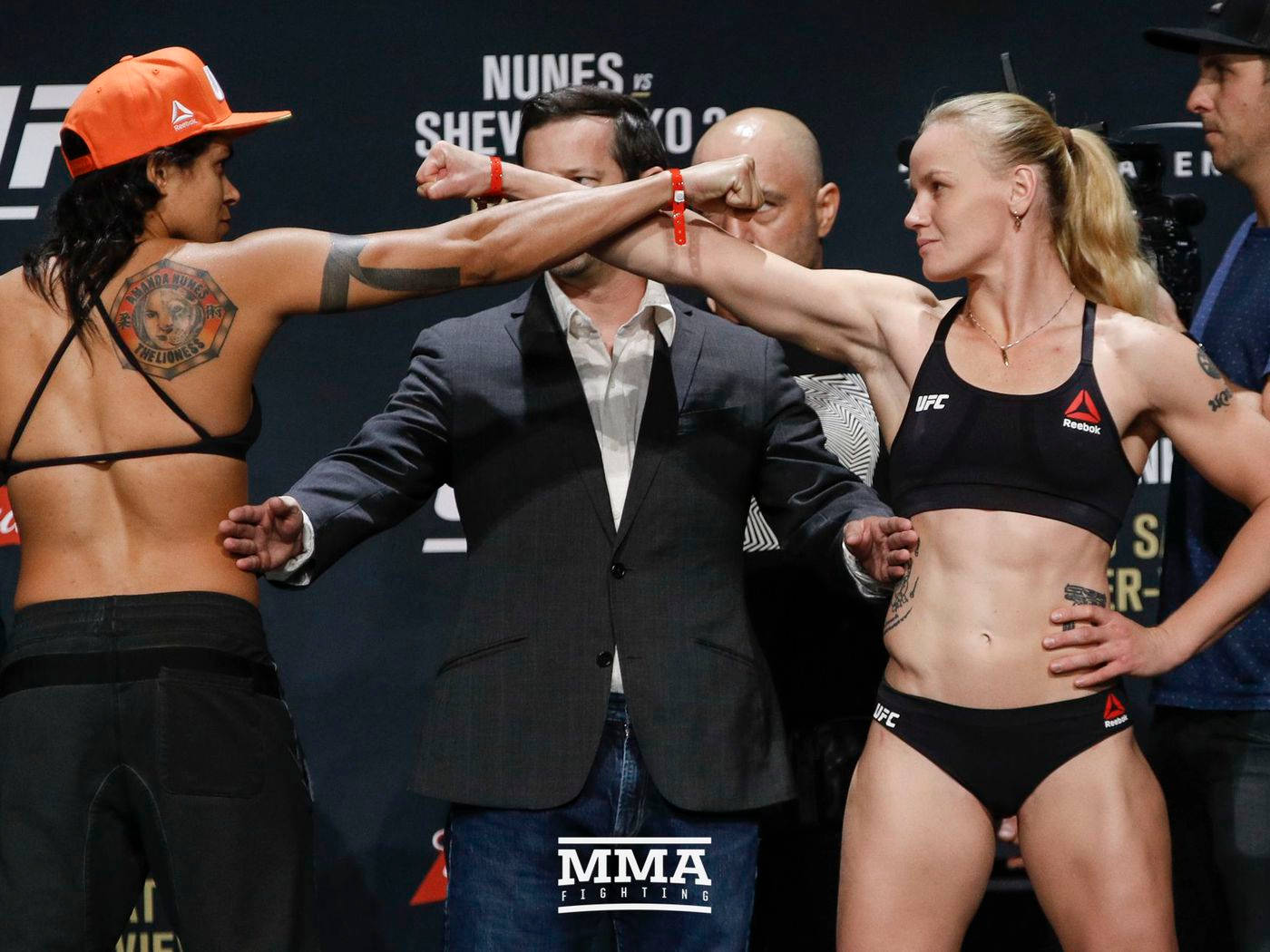 UFC 桌布 壁紙 — 兩名身穿黑色裝備的女子MMA拳手在稱重活動中鎖拳，中間有裁判。