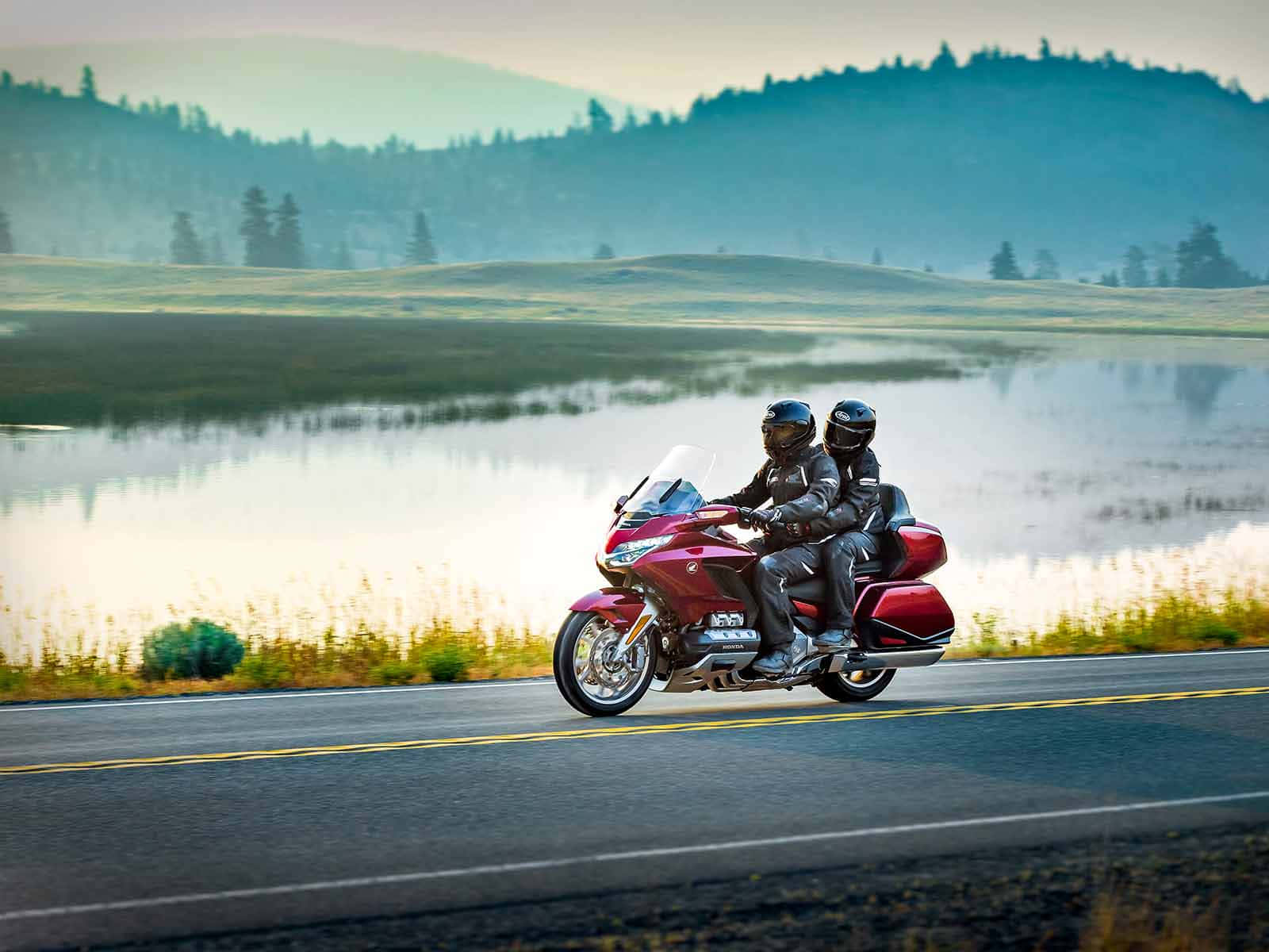 biker 桌布 壁紙 — 兩名身穿黑色裝備的騎士，騎著一輛紅色旅行摩托車，沿著霧氣瀰漫的湖邊道路行駛，背景是森林覆蓋的山丘。