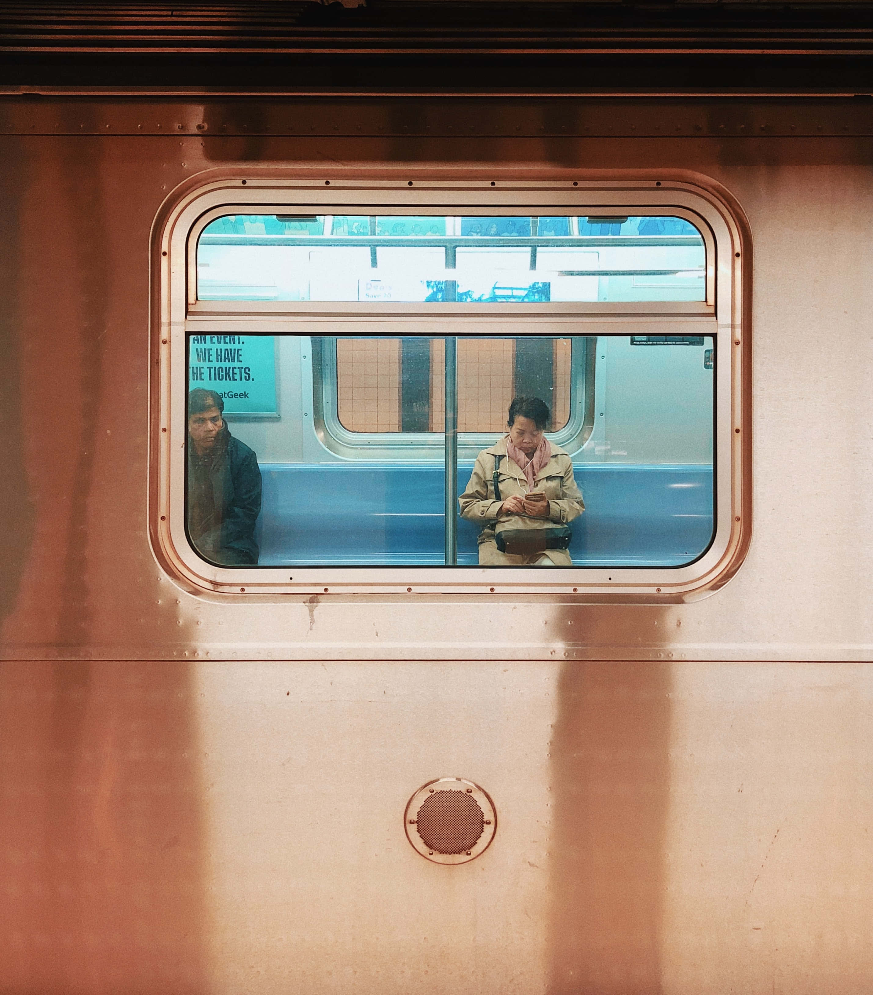 Bronze 桌布 壁紙 — 兩名通勤者坐在火車車廂內，透過圓形車窗觀看，車廂帶有溫暖的金屬色調和藍色座椅。