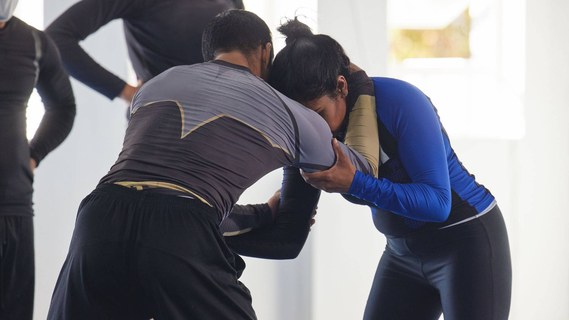 martial arts 桌布 壁紙 — 兩名運動員在明亮的室內訓練室中激烈纏鬥，其他人在旁觀看。