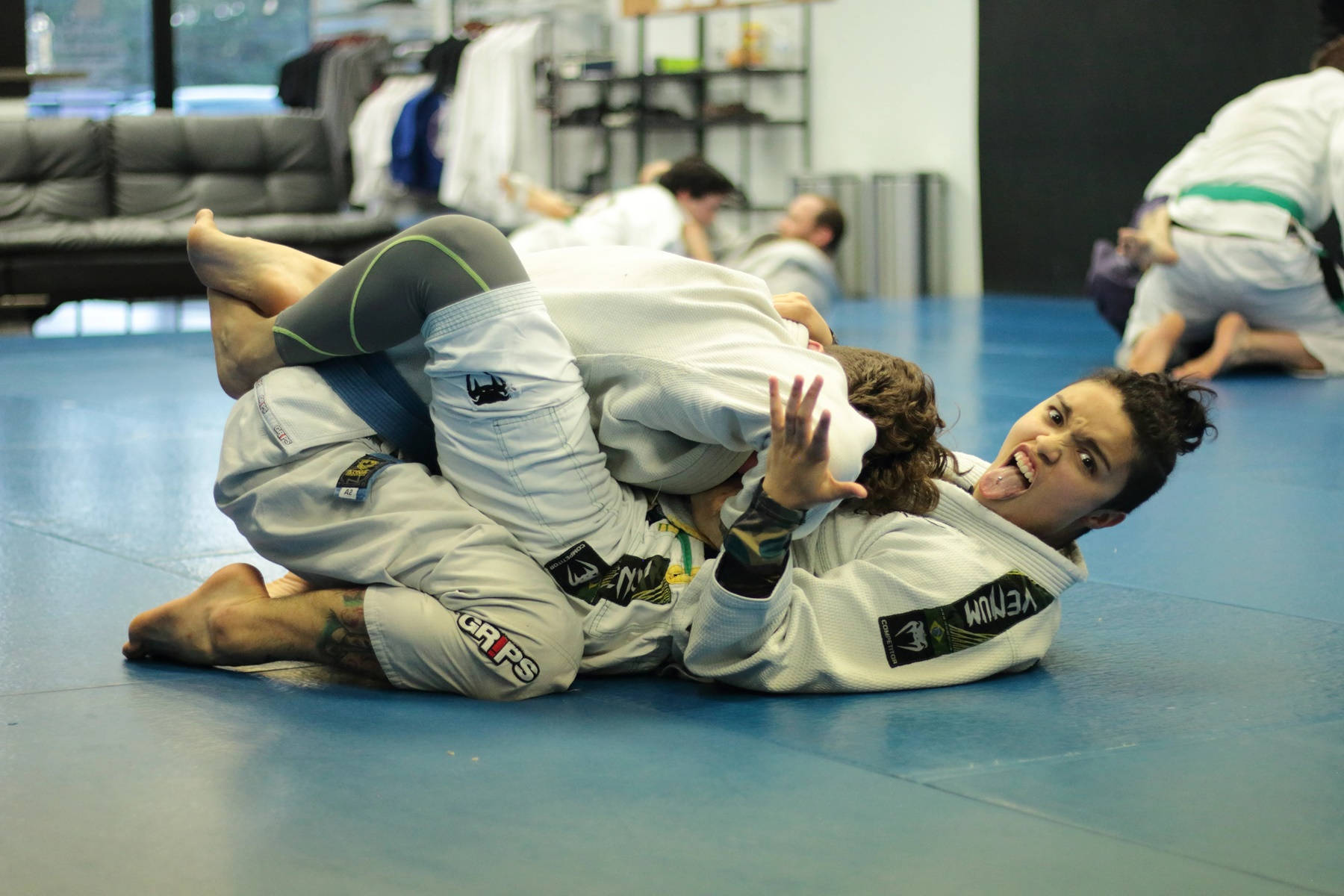 martial arts 桌布 壁紙 — 兩名運動員在藍色軟墊上激烈纏鬥，背景中還有其他人在武術館訓練。