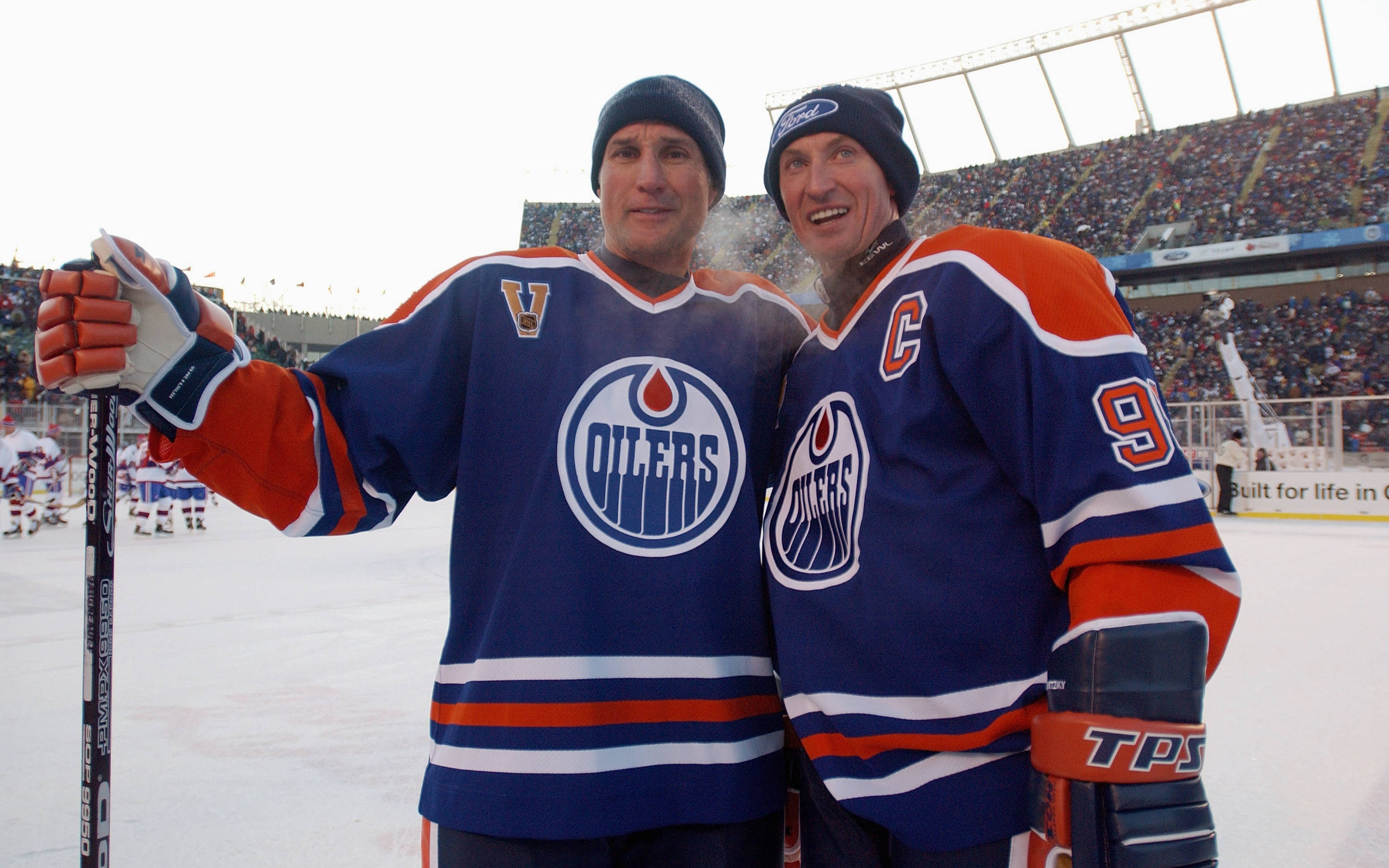 Oilers 桌布 壁紙 — 兩名面帶微笑的埃德蒙頓油人冰球球員身穿藍橙色球衣，在冰上與背景中的球迷合影。