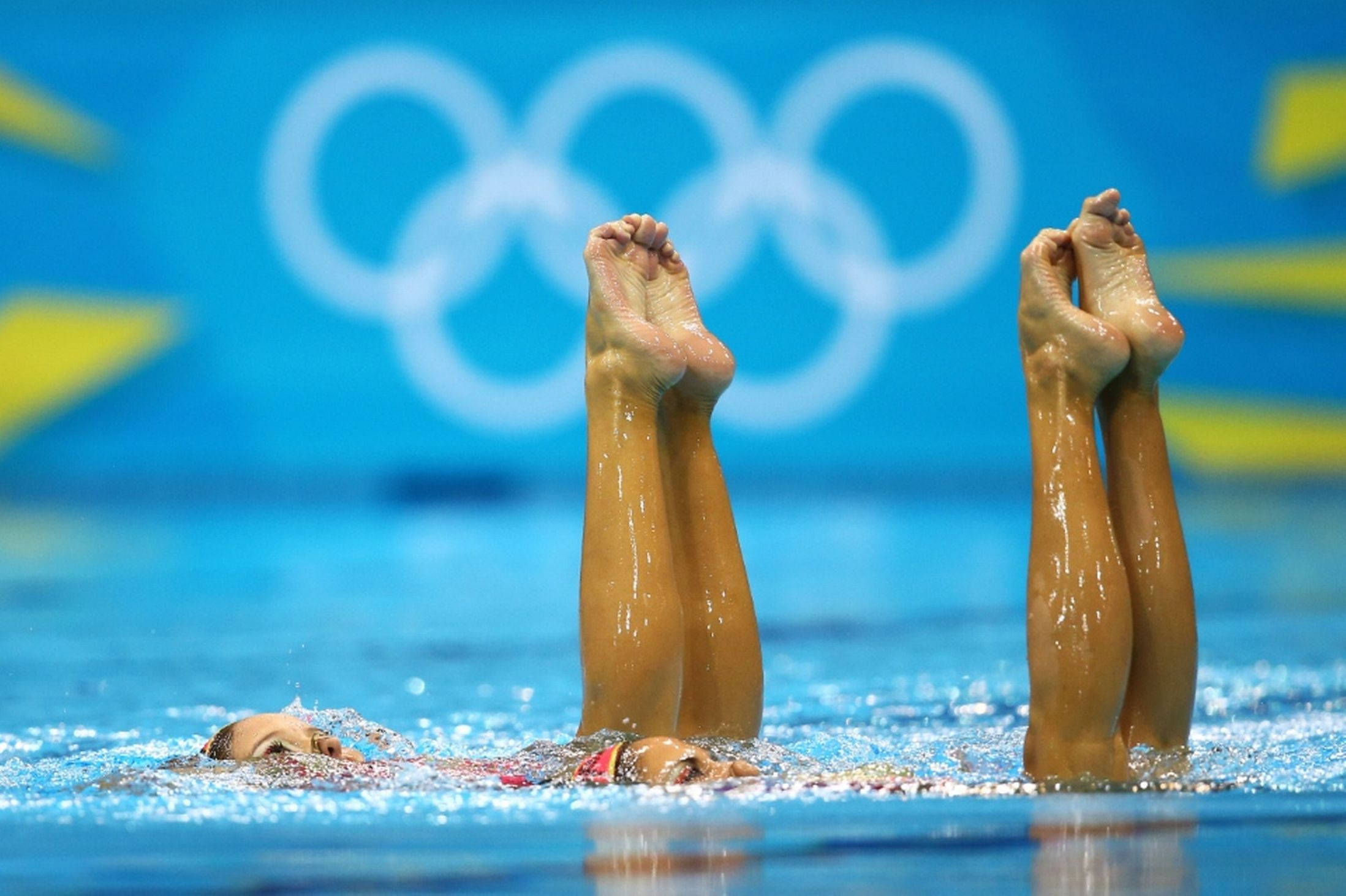 Swimming 桌布 壁紙 — 兩名韻律泳選手在奧運五環背景下表演抬腿動作。