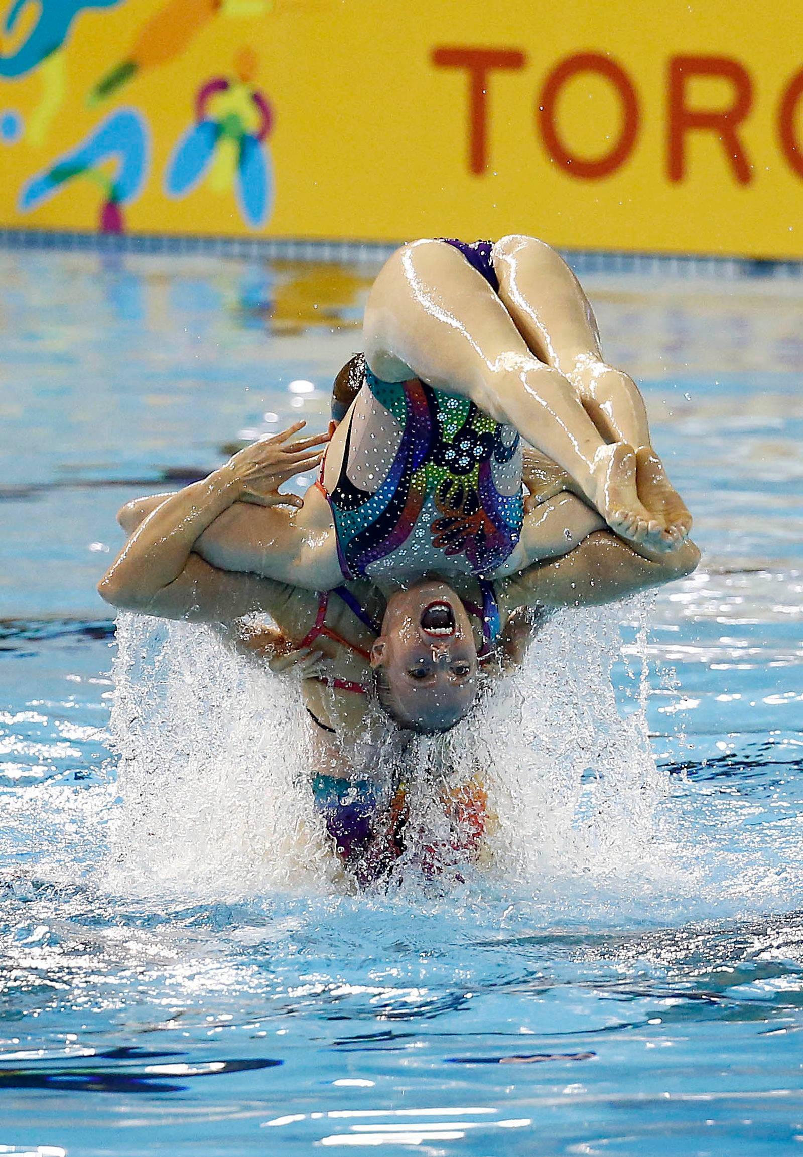 Swimming 桌布 壁紙 — 兩名韻律泳選手在泳池中執行戲劇性的高舉動作，背景是充滿活力的多倫多。