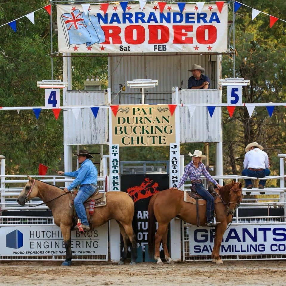 Rodeo 桌布 壁紙 — 兩名騎馬的牛仔在納蘭德拉牛仔競技表演的騎牛閘旁，在節日橫幅下準備就緒。