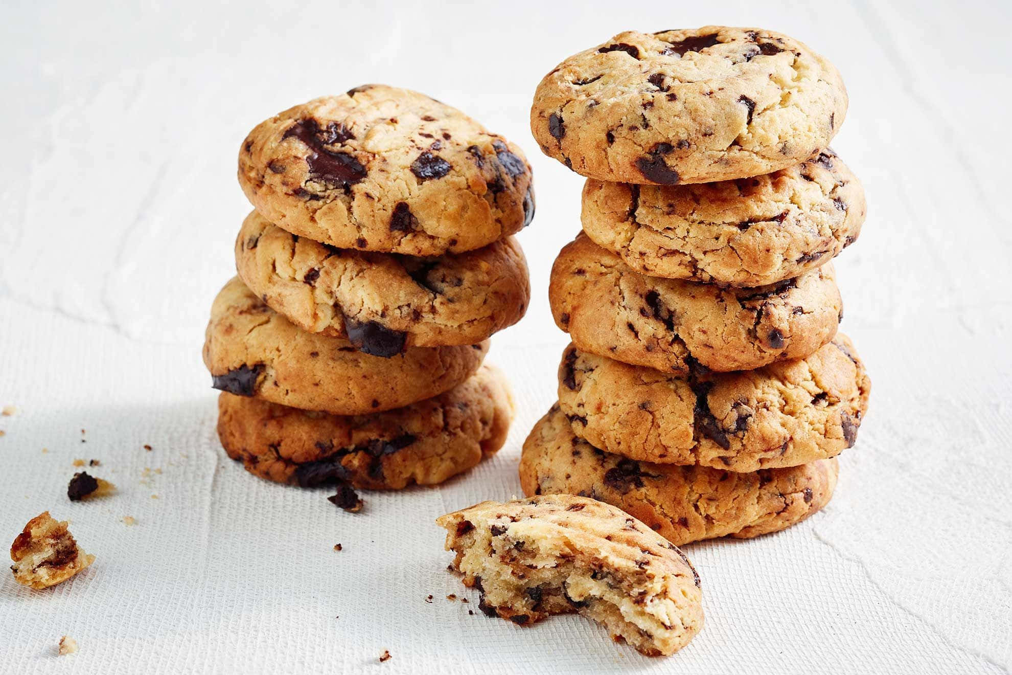 Biscuit 桌布 壁紙 — 兩堆金黃色巧克力片餅乾，其中一塊碎裂的在前面，放在白色紋理表面上。