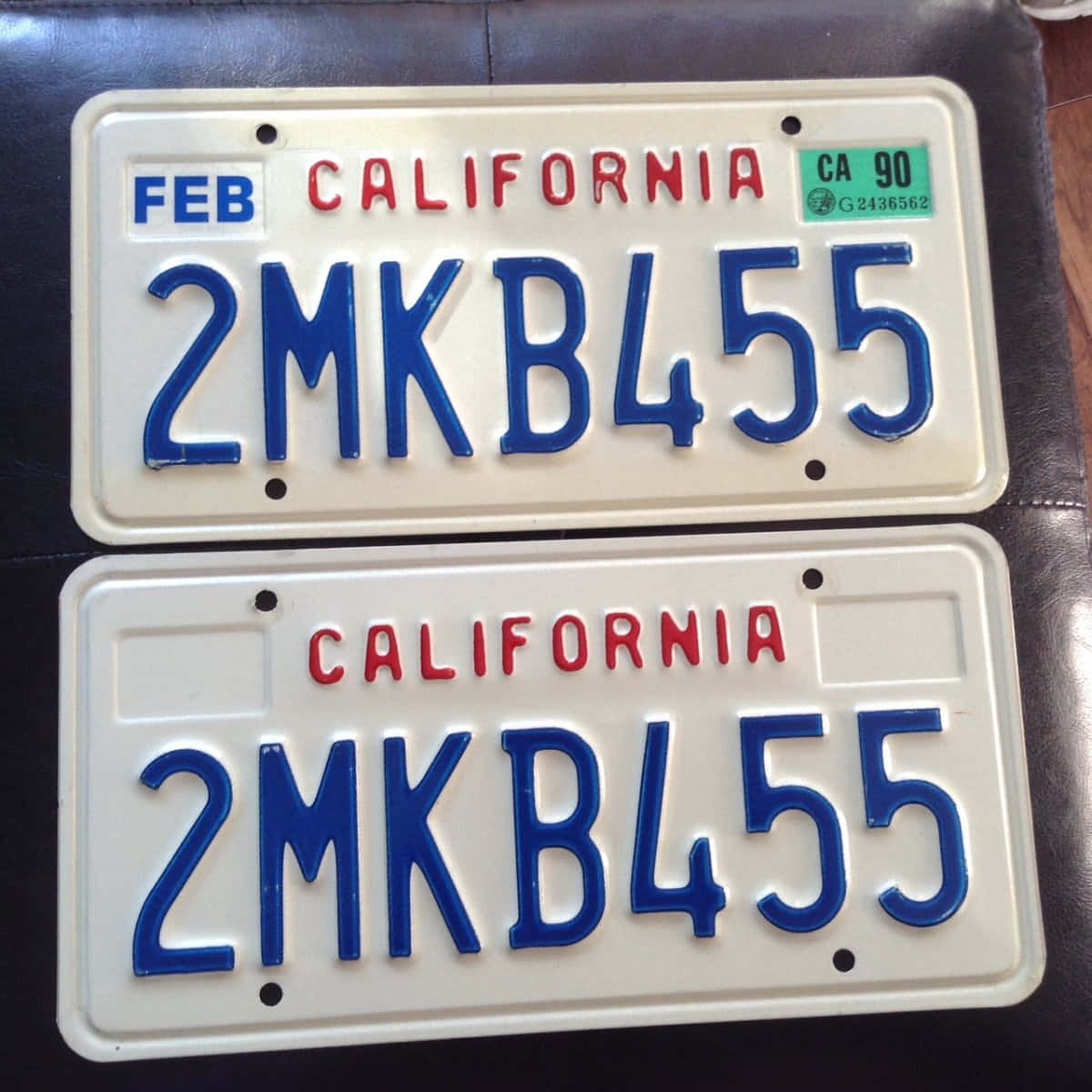 License Plate 桌布 壁紙 — 兩塊加州車牌，帶有藍色字母和紅色州名，放置在深色皮革表面上。